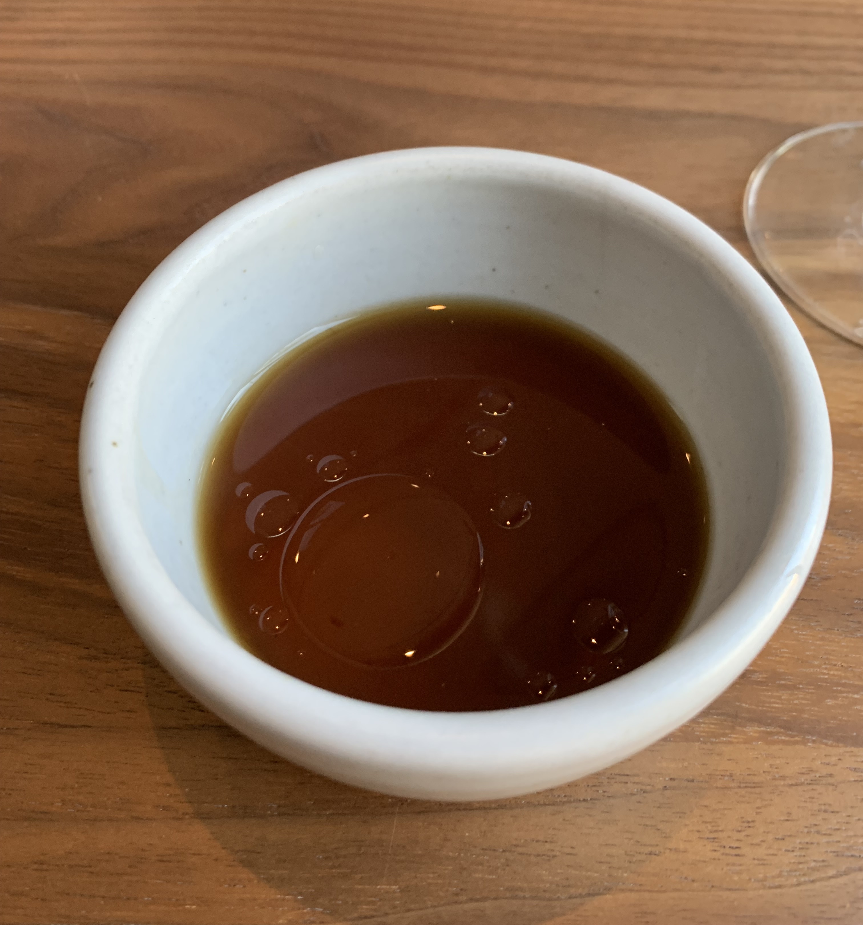 Shallow bowl of dark brown tea, with a few big drops of oil floating on the top
