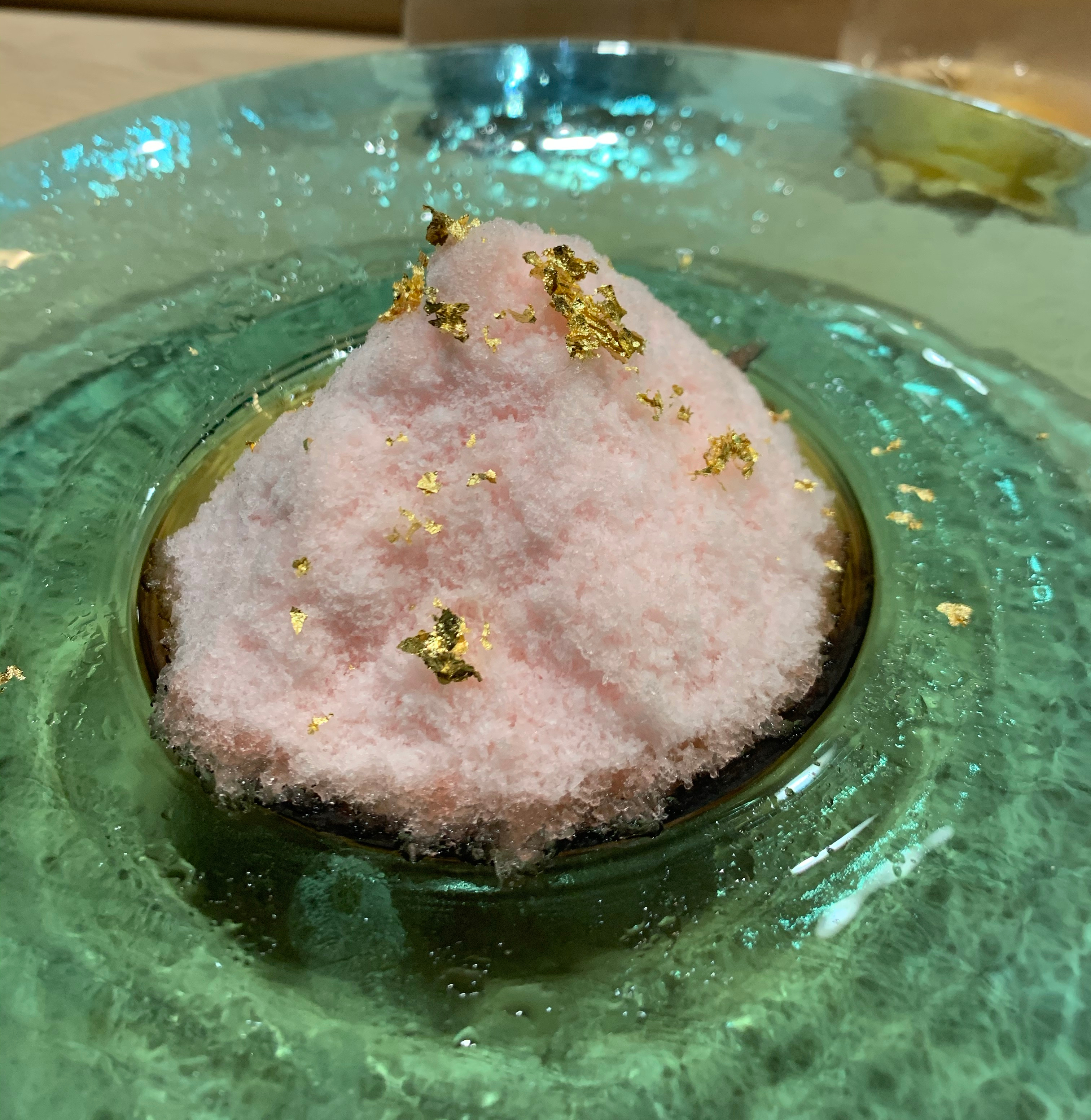 Very finely-shaved ice, coloured pink, with gold flakes served in a wide green bowl.