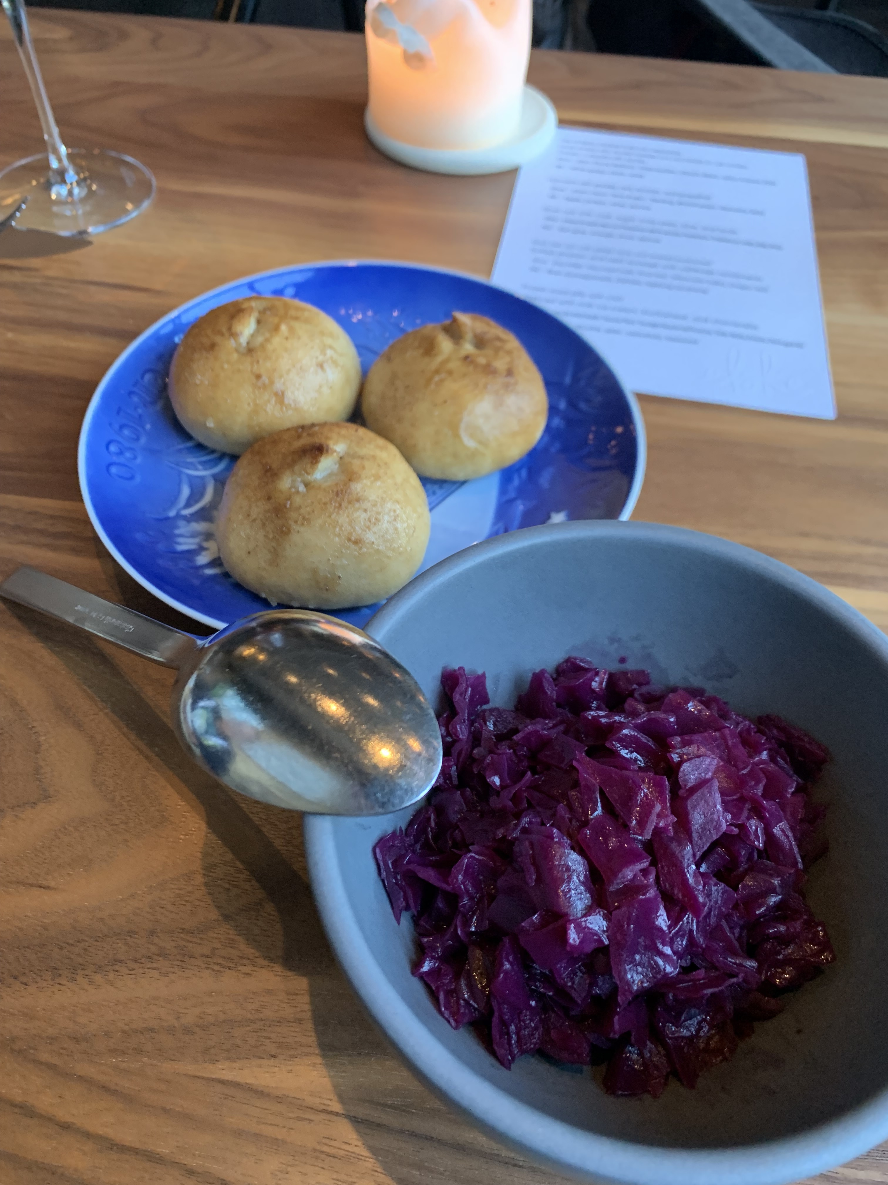 Three little rolls served on a blue plate, with a dark powder topping them. A nearby bowl has pickled red cabbage.