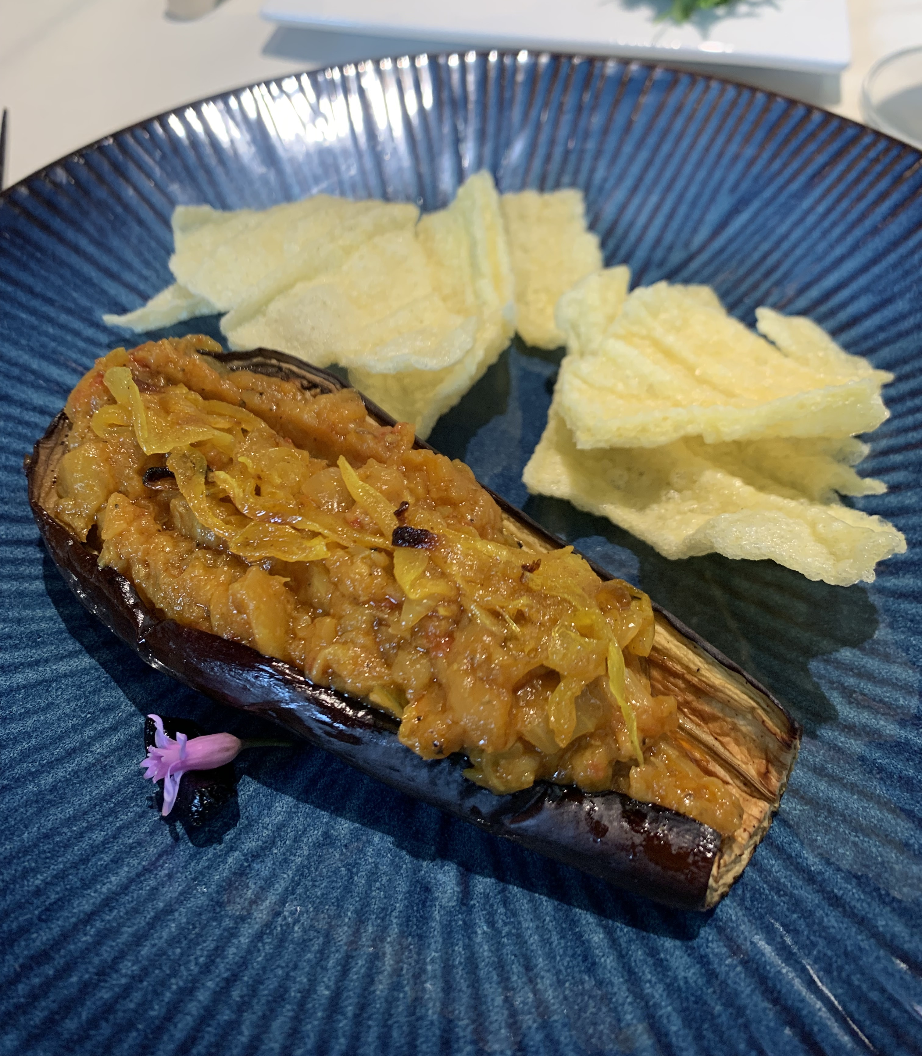 An eggplant that's has its insides scooped out, added to, and put back in. The filling is a darker shade of orange that it would normally be. There are some pale chips next to it.