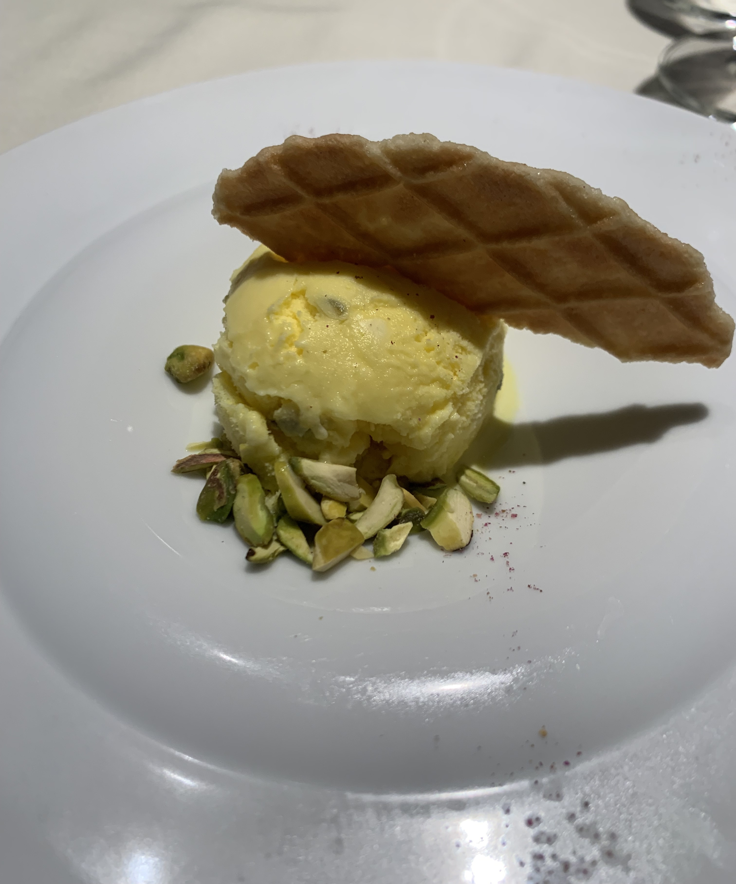 Scoop of yellow ice cream with a shard of waffle cone sticking out of it. A few chopped pistachios surround the ice cream.