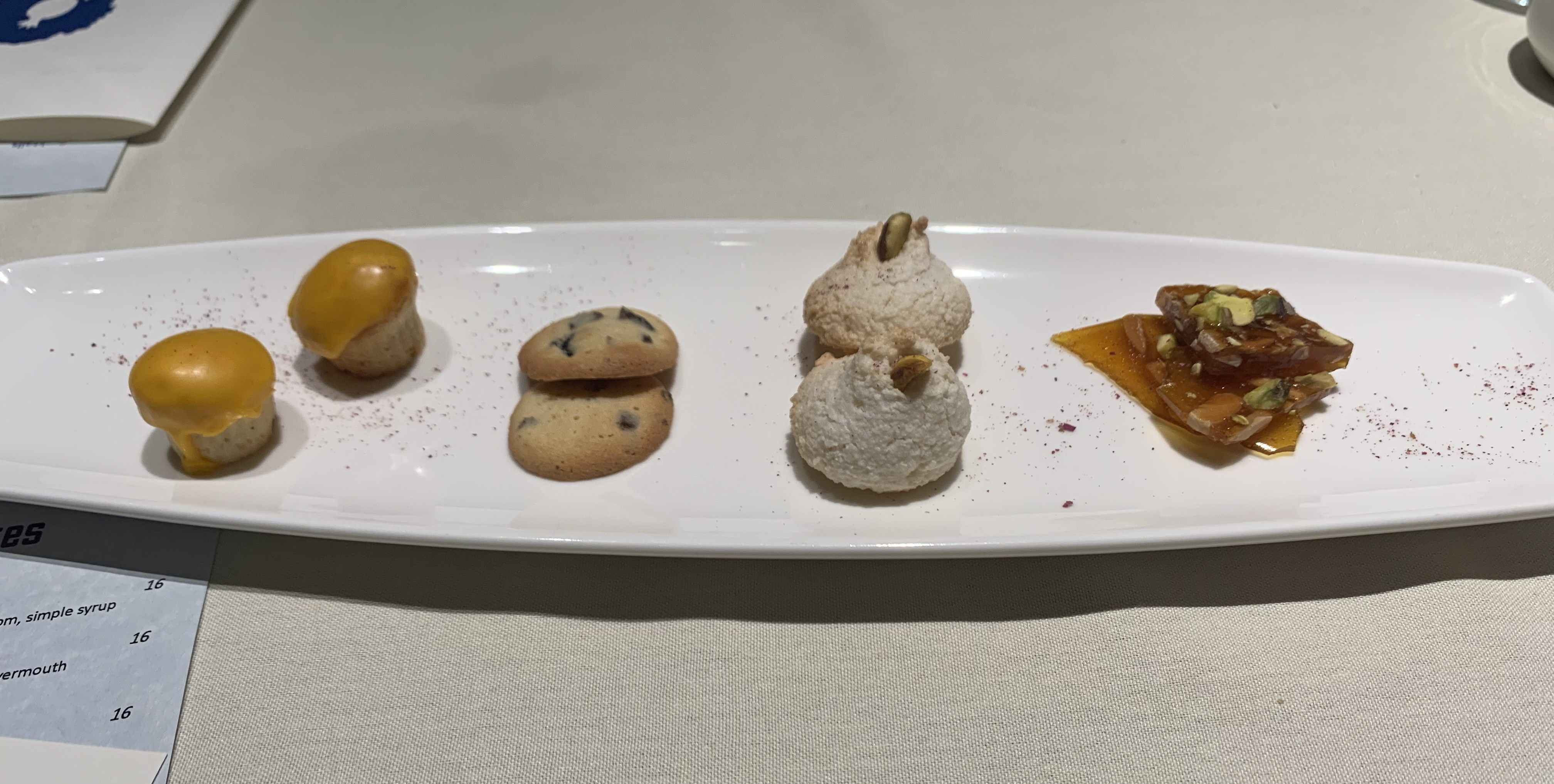 Plate with four confections: a muffin-looking thing with a golden glaze on top, a typical cookie, a cookie that looks like it has powdered sugar all over it, and translucent amber bark with nuts embedded in it.