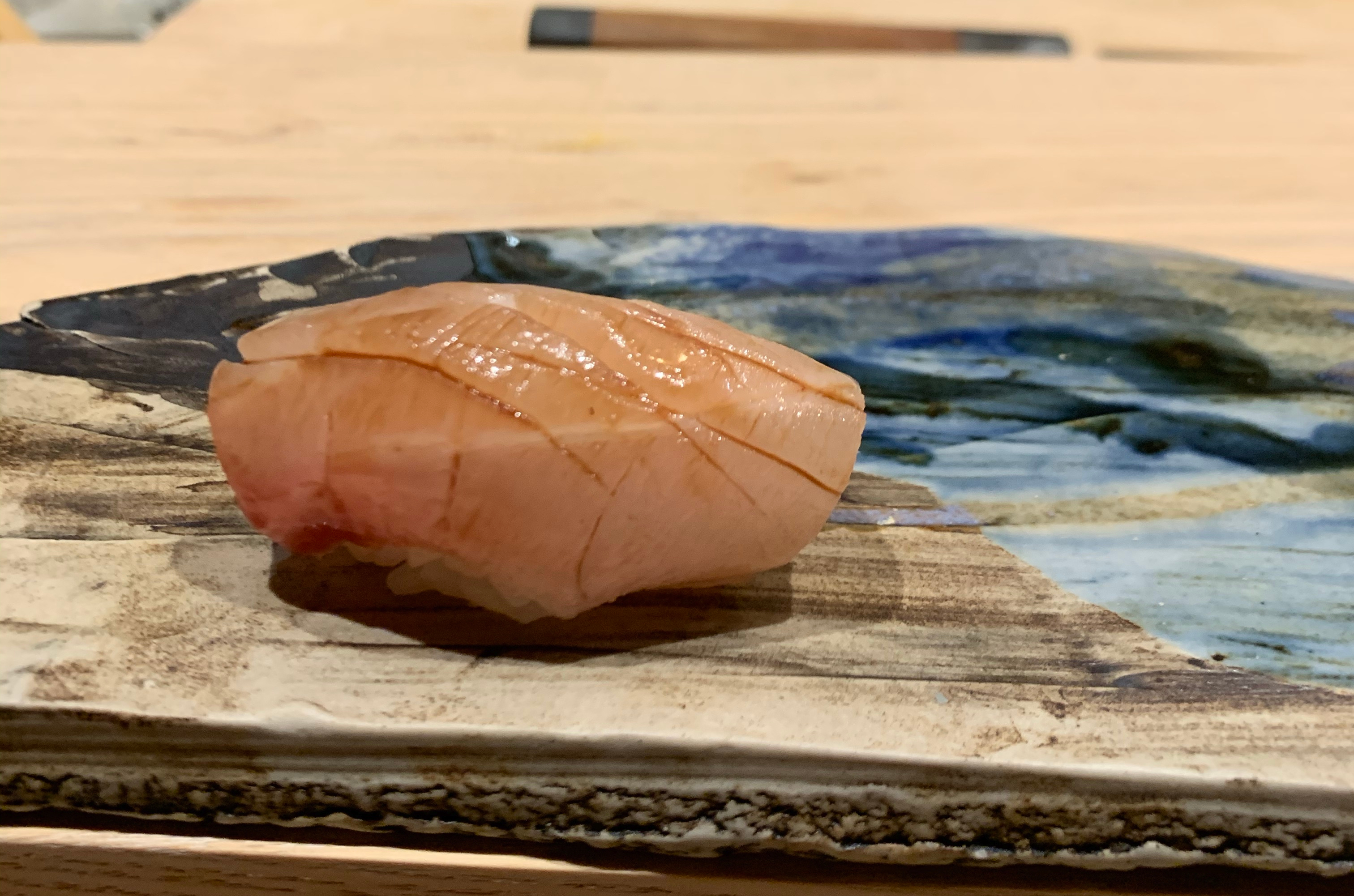 One piece of nigiri sushi with a white fish. The fish has been brushed lightly with soy sauce, which has pooled in the gaps between the muscles, giving it a look like it's been drawn on