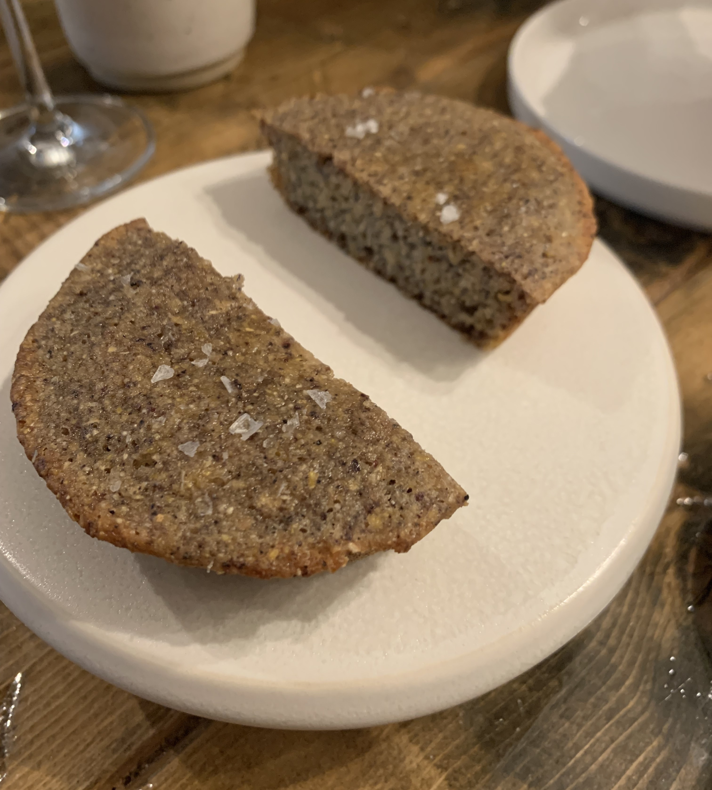 Round corn bread sliced into two portions. The bread is a dark brown with blue speckles, and there are some big flaky bits of salt on top.