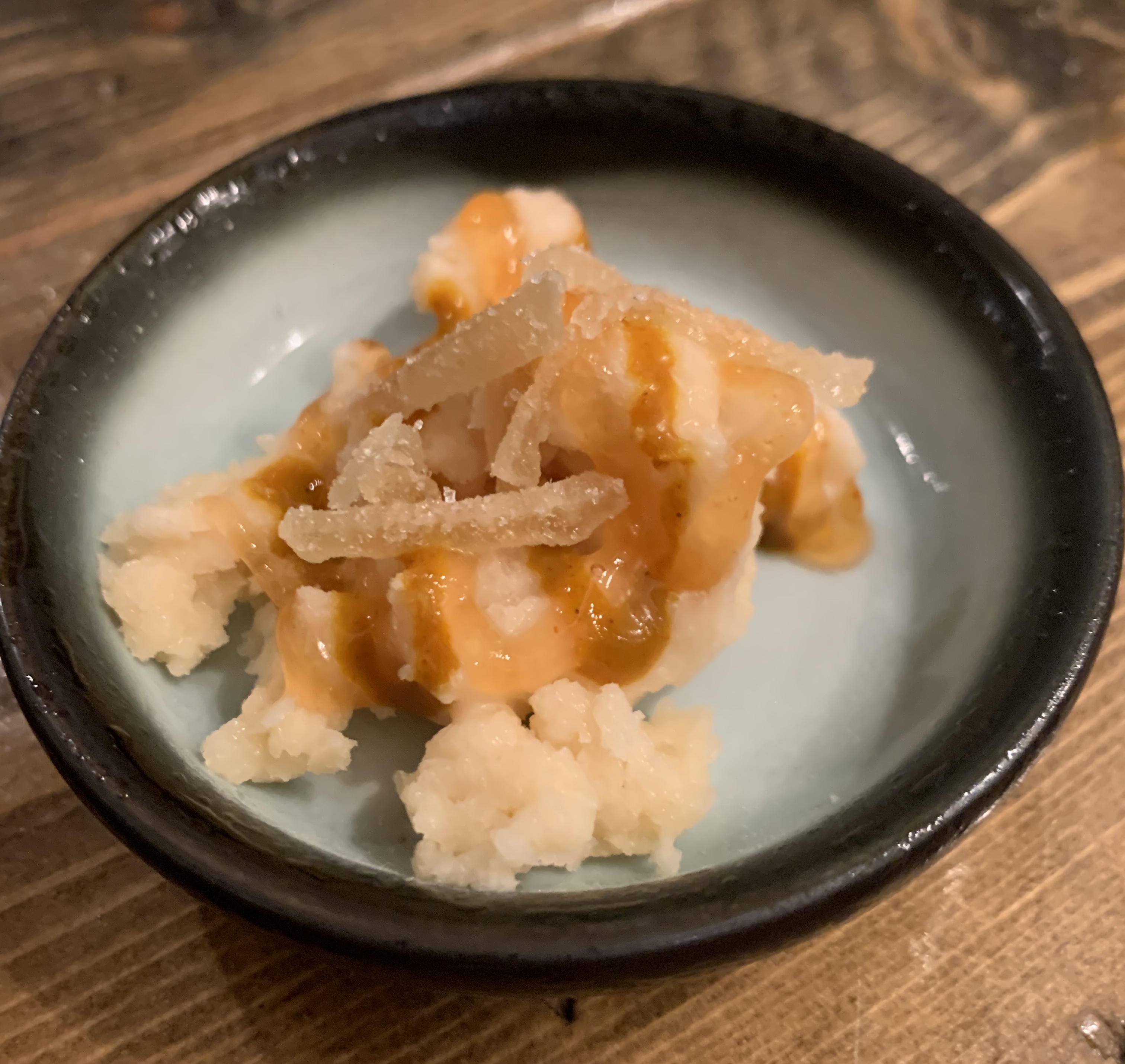 Tiny bowl of shaved ice, with some bits of crystalized ginger and an orange sauce