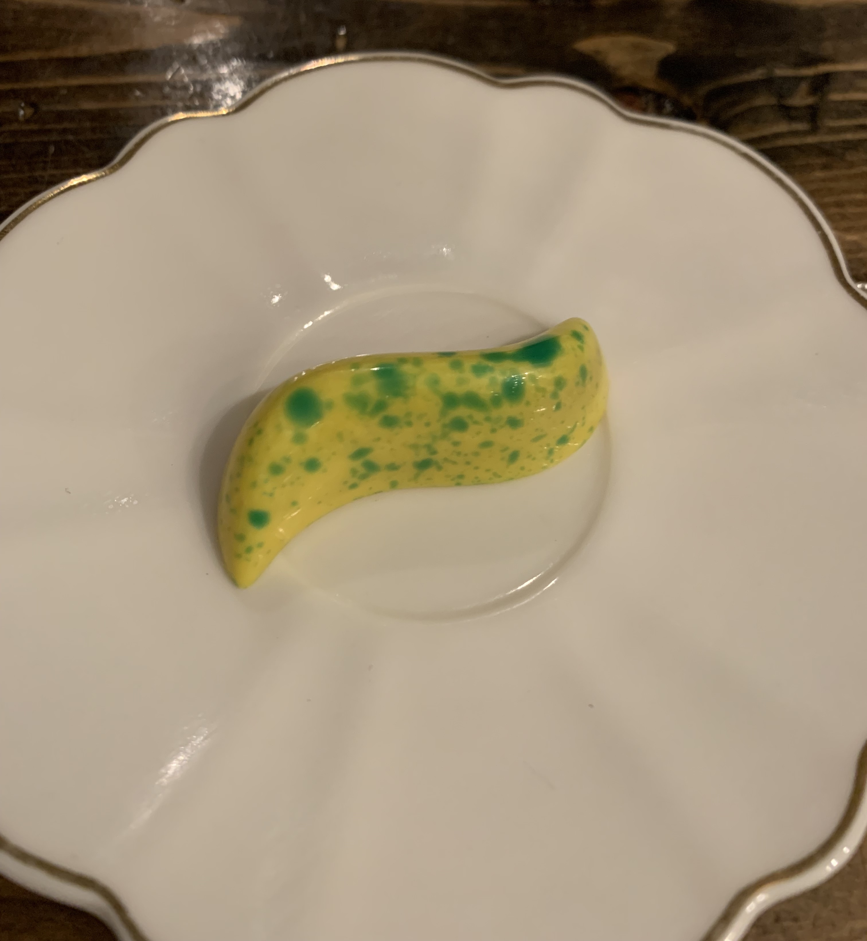 A single bonbon shaped like a slash, with the ends curved. It's shiny and yellow, with green speckles.