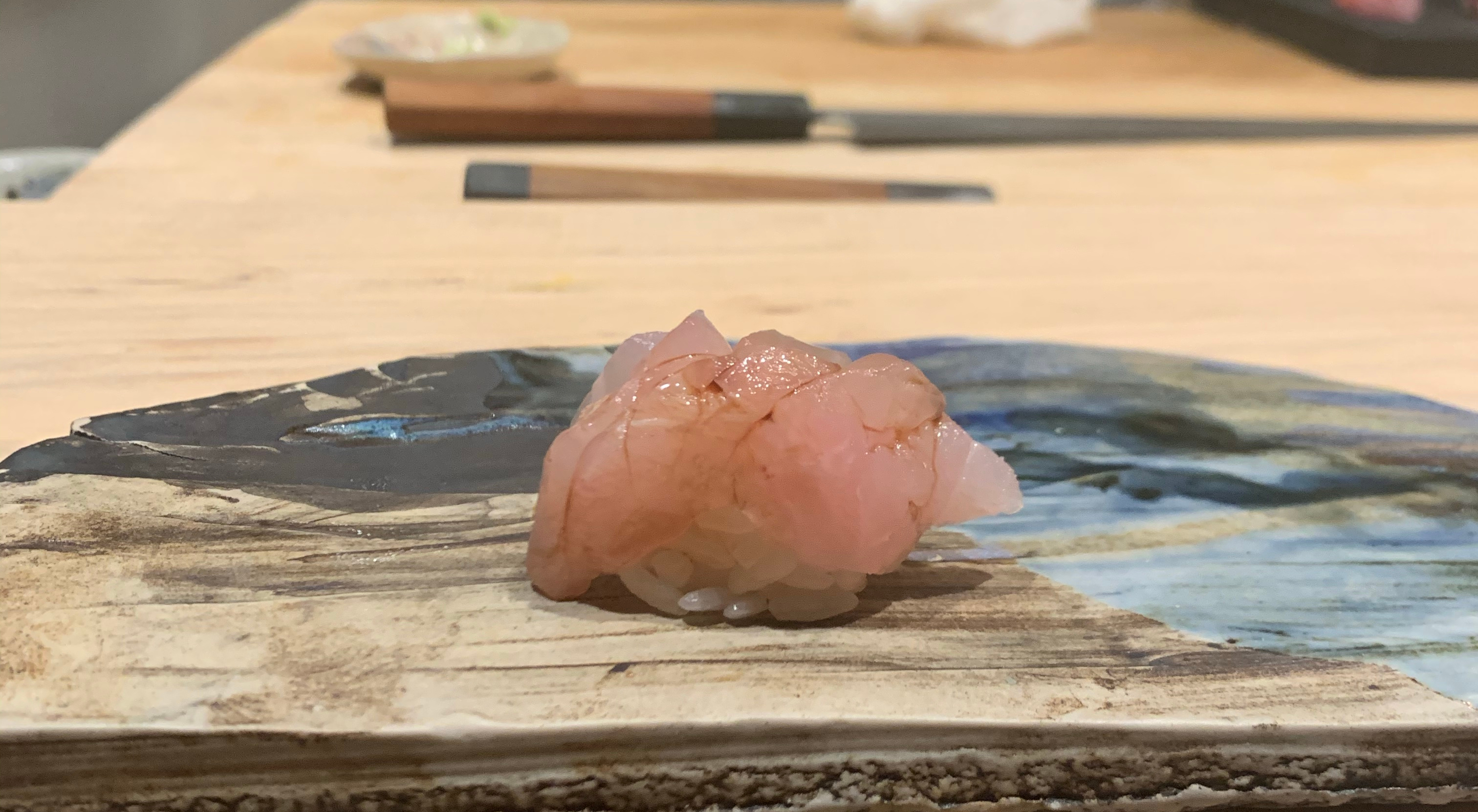 One piece of nigiri sushi with a white fish on top. The fish has been brushed with soy sauce lightly.