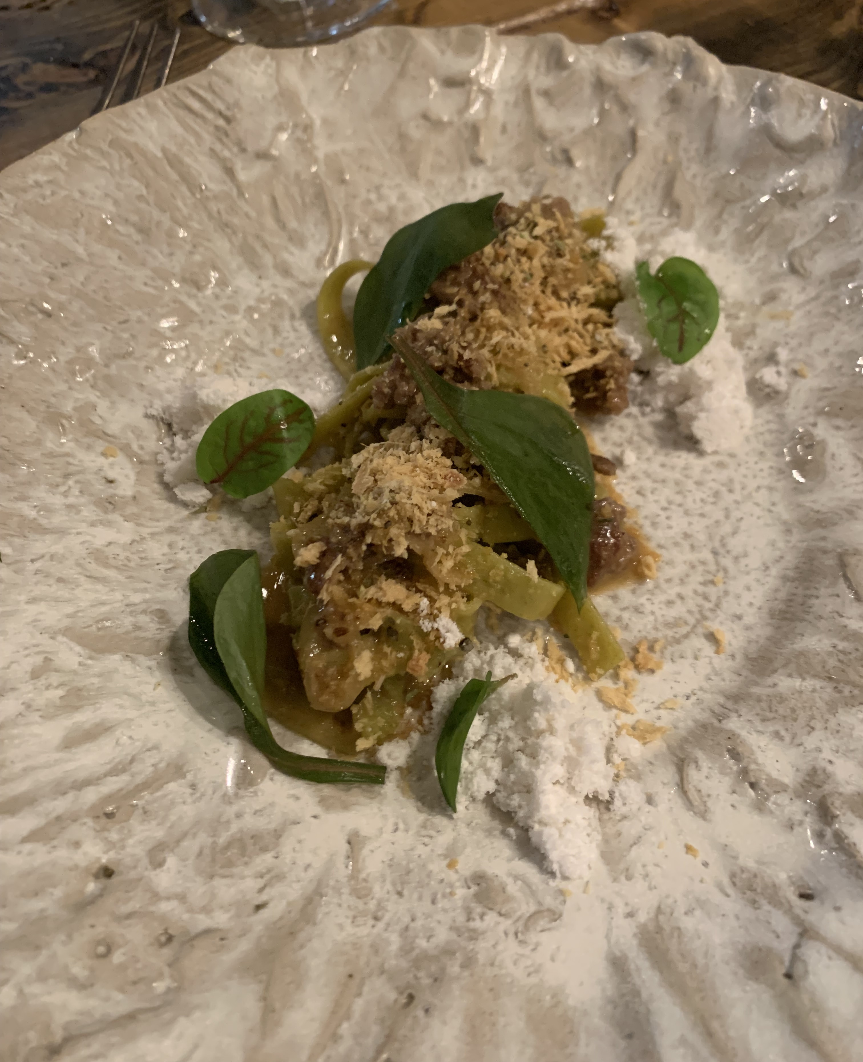 Tightly-coiled thin noodles, green in hue, served covered in crunchy bits, and garnished with beautiful green leaves. There are dark chunks of lamb sausage peeking out from underneath everything.