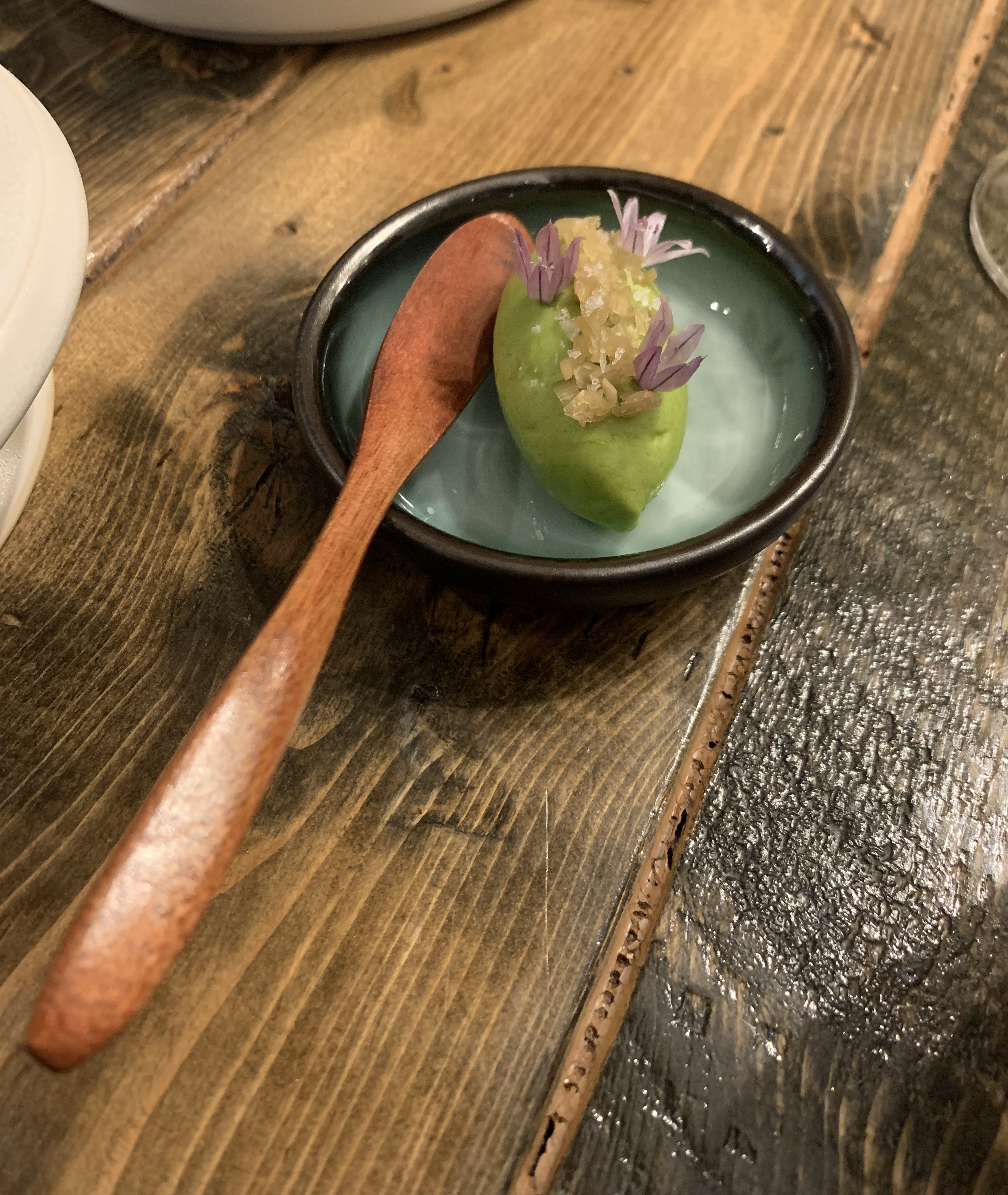 Quenelle of green butter, topped with small purple flowers. Served on a tiny round plate with a lacquered wooden paddle for spreading.