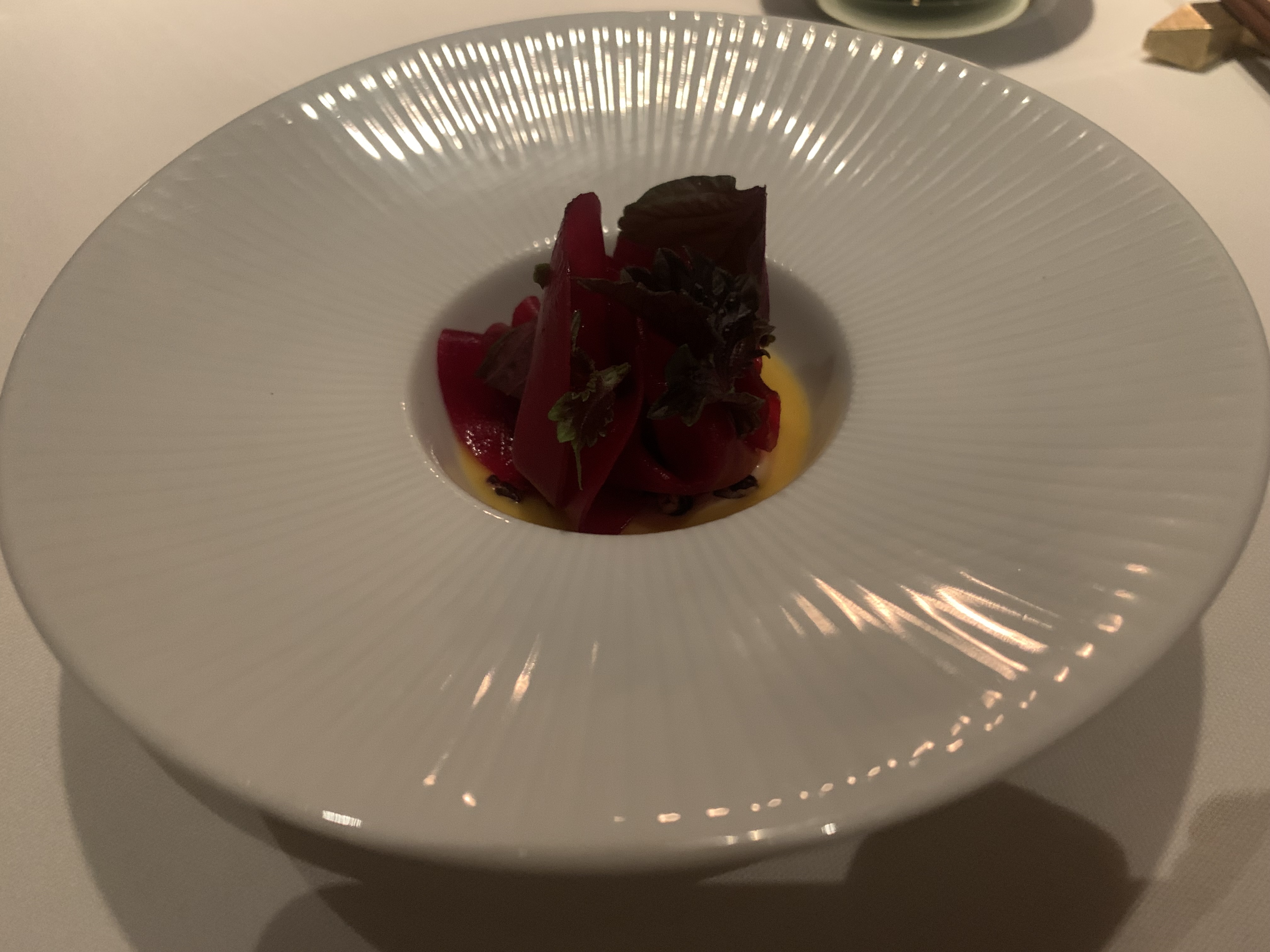White bowl with a heaping mound of shaved, dark-red beets sitting atop a dark orange sauce.