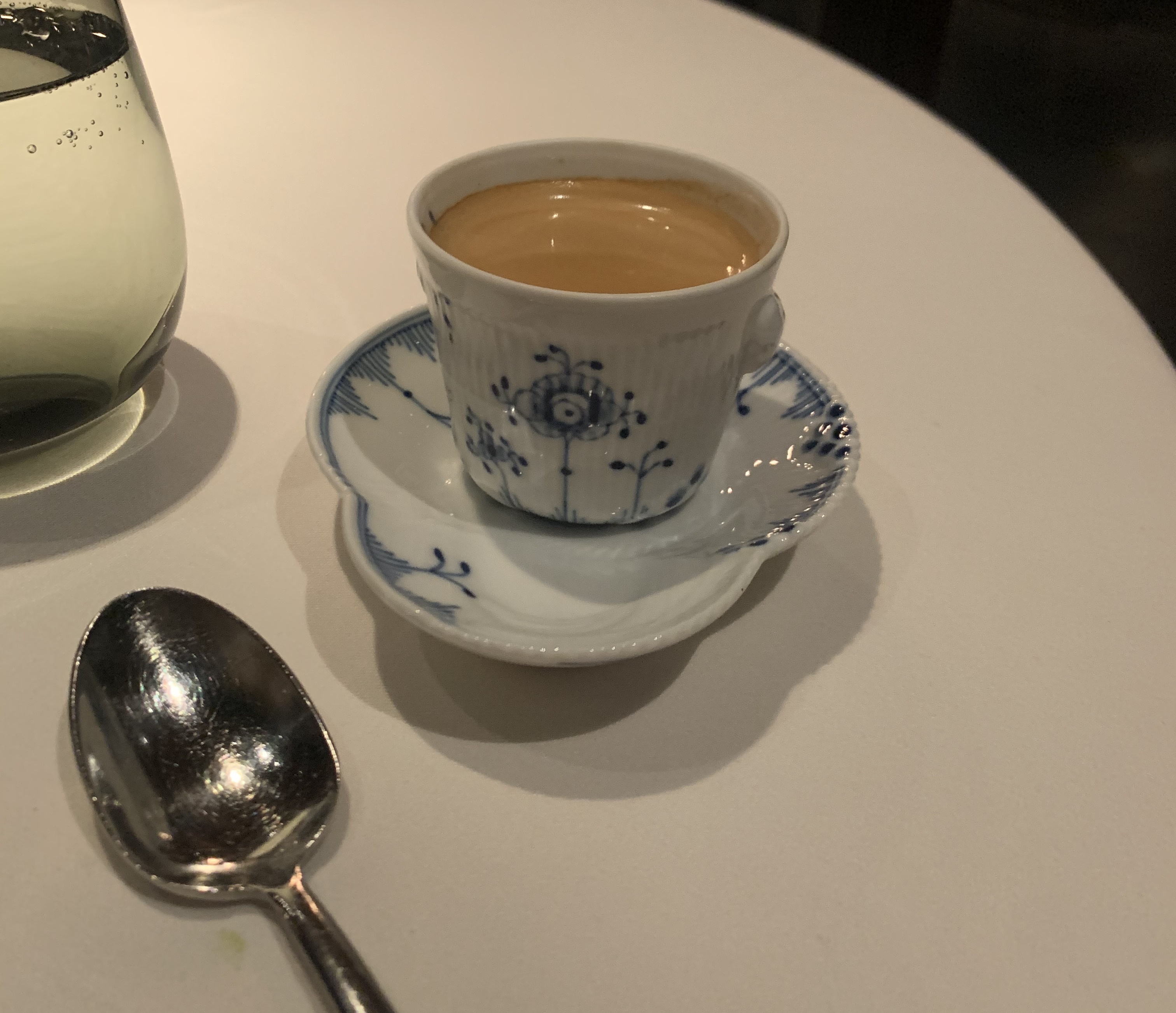 Espresso with a light head in a tiny porcelain cup, accented with abstract blue designs that look vaguely like trees. It's on an oddly-shaped saucer with the same blue designs.