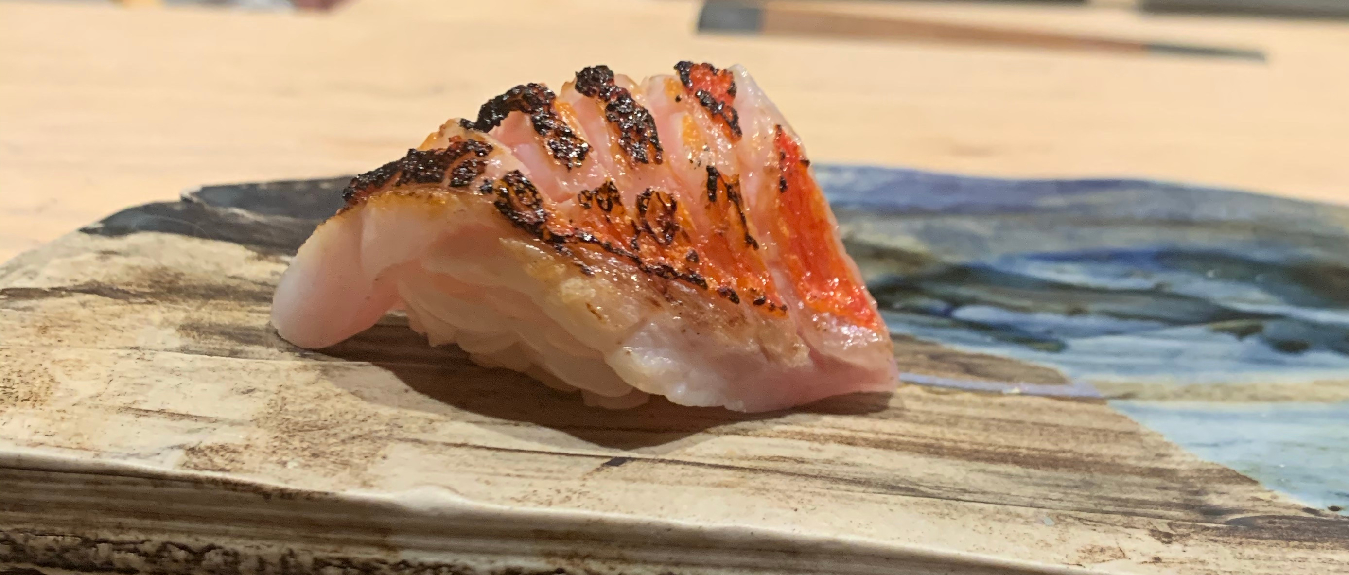 One piece of nigiri sushi, with a white fish that has been charred along slightly-raised natural ridges