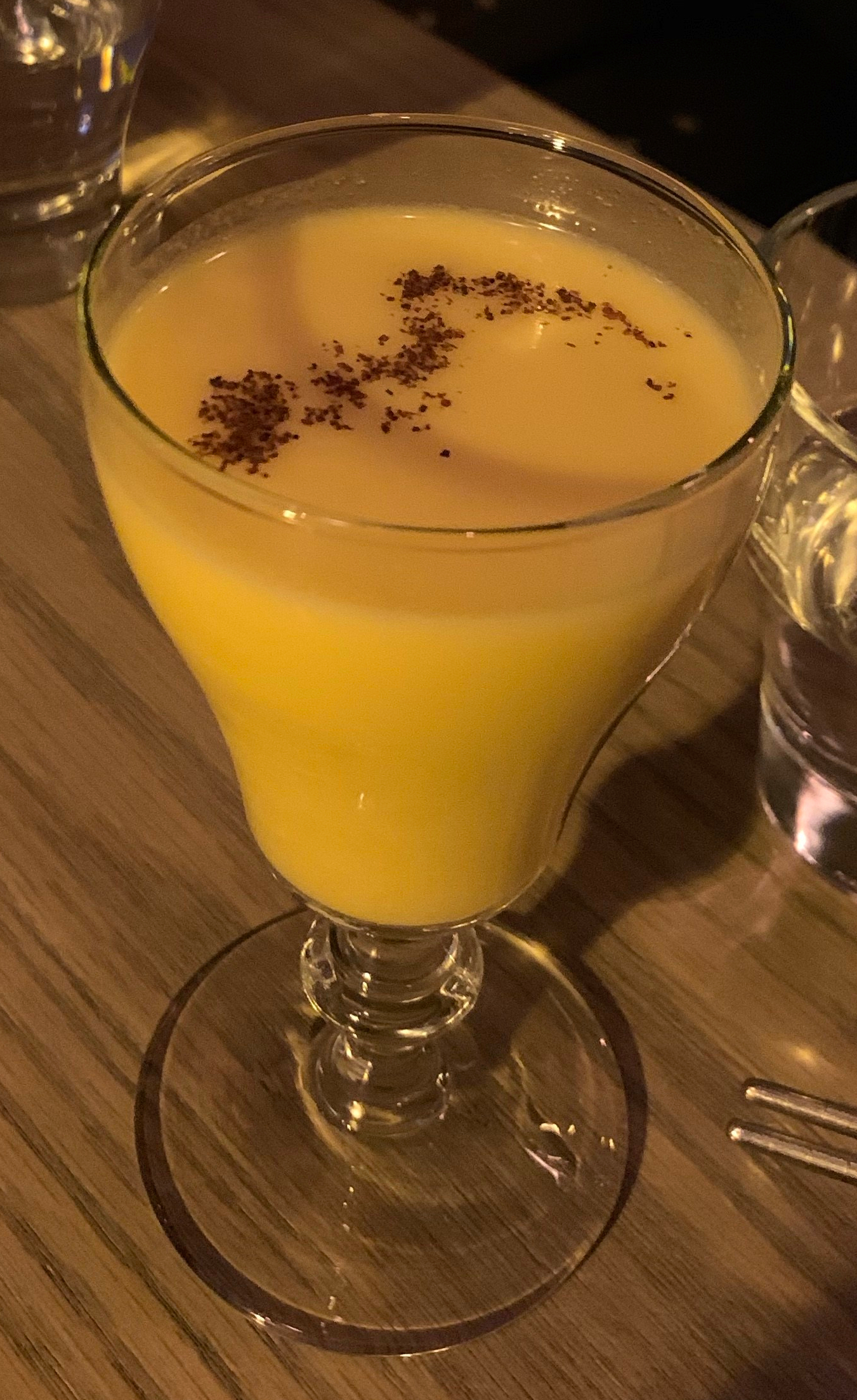 An orange-ish fluid in a cocktail glass, with some spices on top