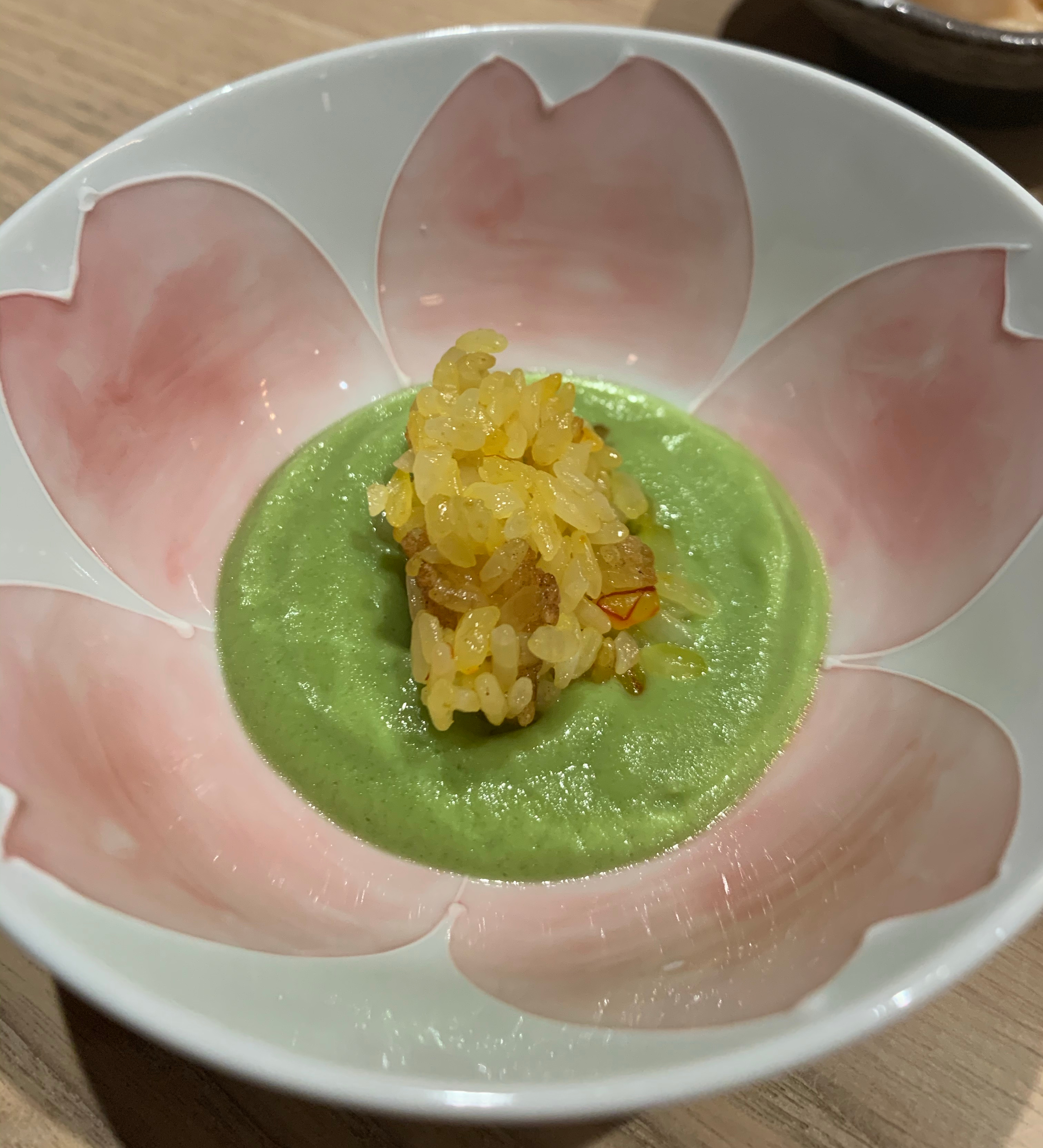 Large bowl with a vaguely-flower-looking motif. There is a circle of green pea puree, and some yellow-tinted rice is in the center of the puree.