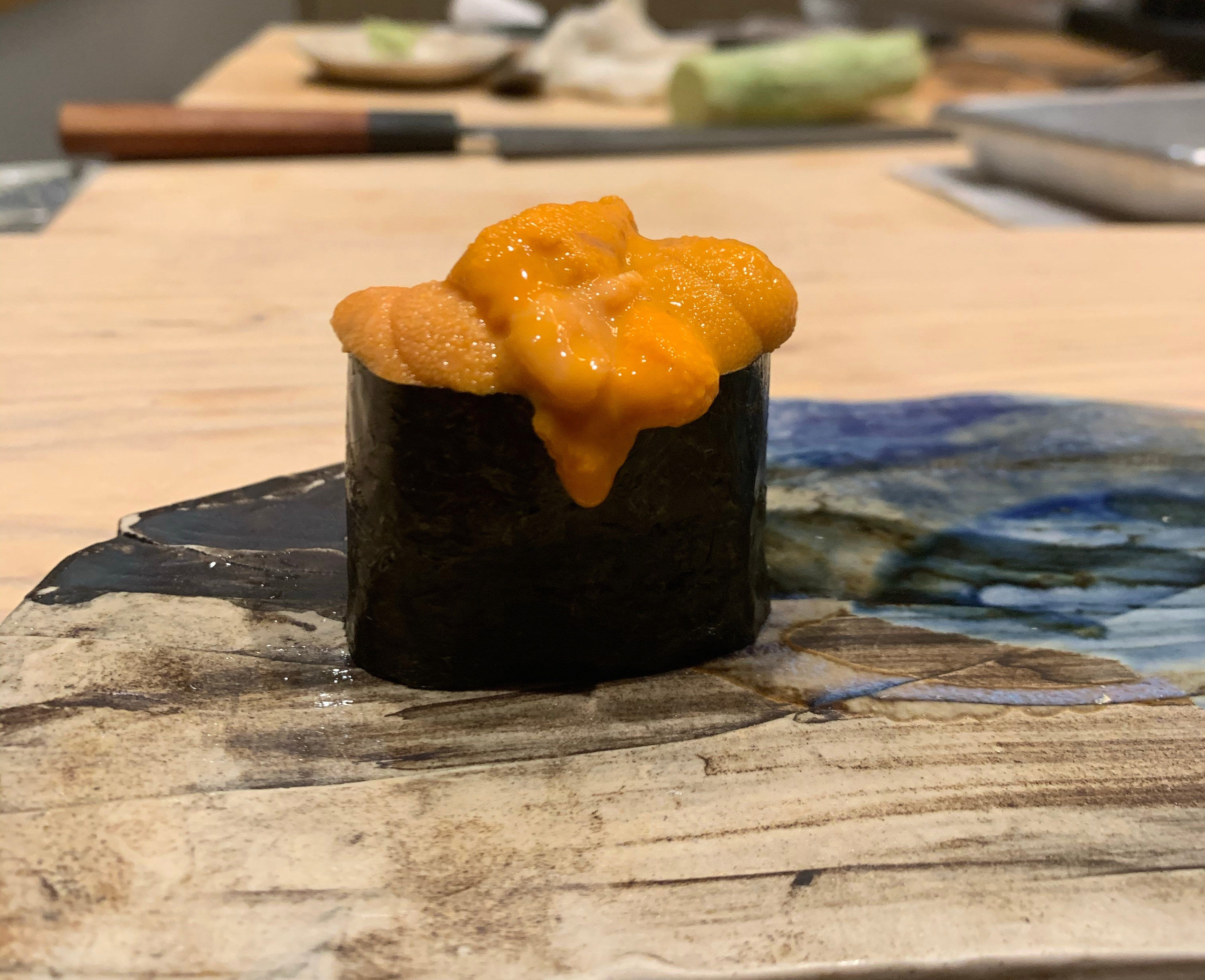 One piece of sushi with orange sea urchin sticking out of the top. There is an orange sauce dripping down the side of the nori. The rice is obscured by the tall nori and the uni.