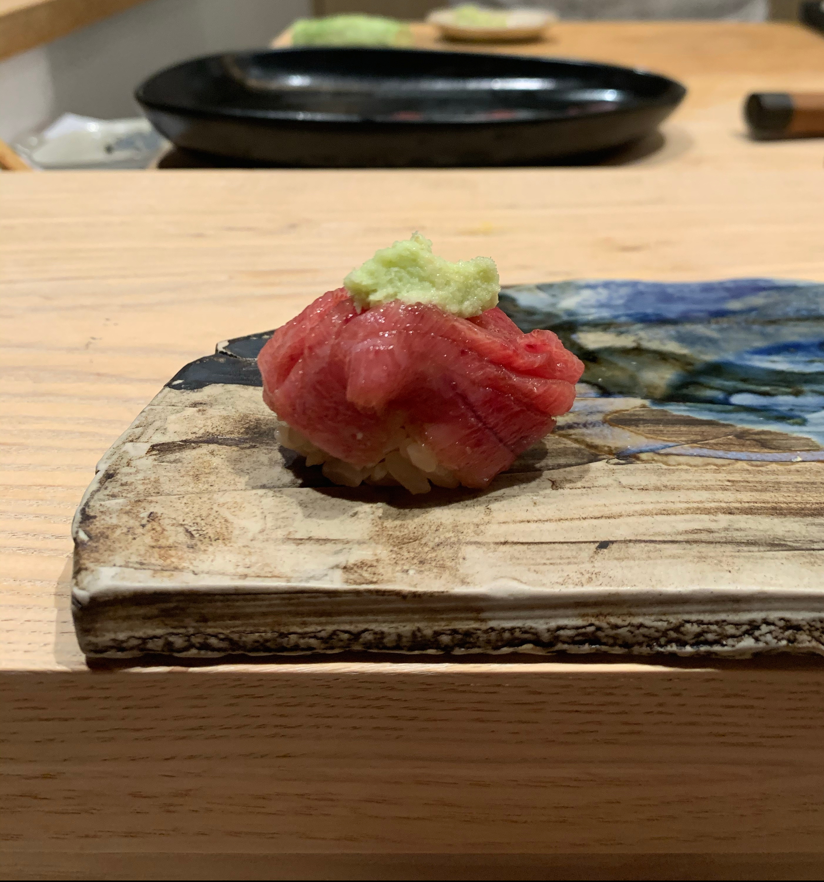 A single piece of nigiri sushi with a red fish on top. The fish has a dollop of pale green wasabi on top of it.
