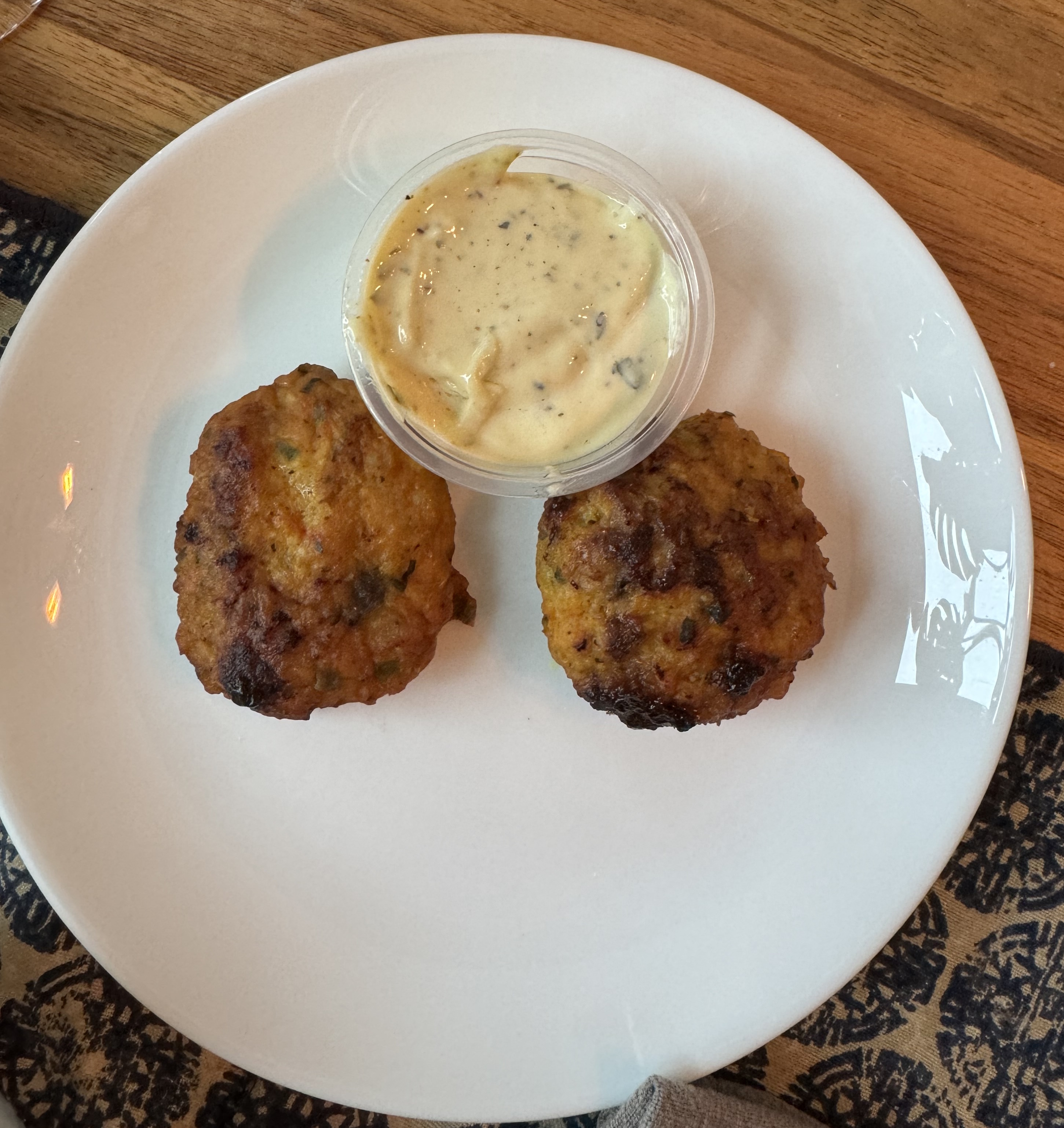 Two dark-brown cakes on a white plate. The cakes are round and a little charred. Between them is a container of creamy sauce: off-white, with flicks of spices.