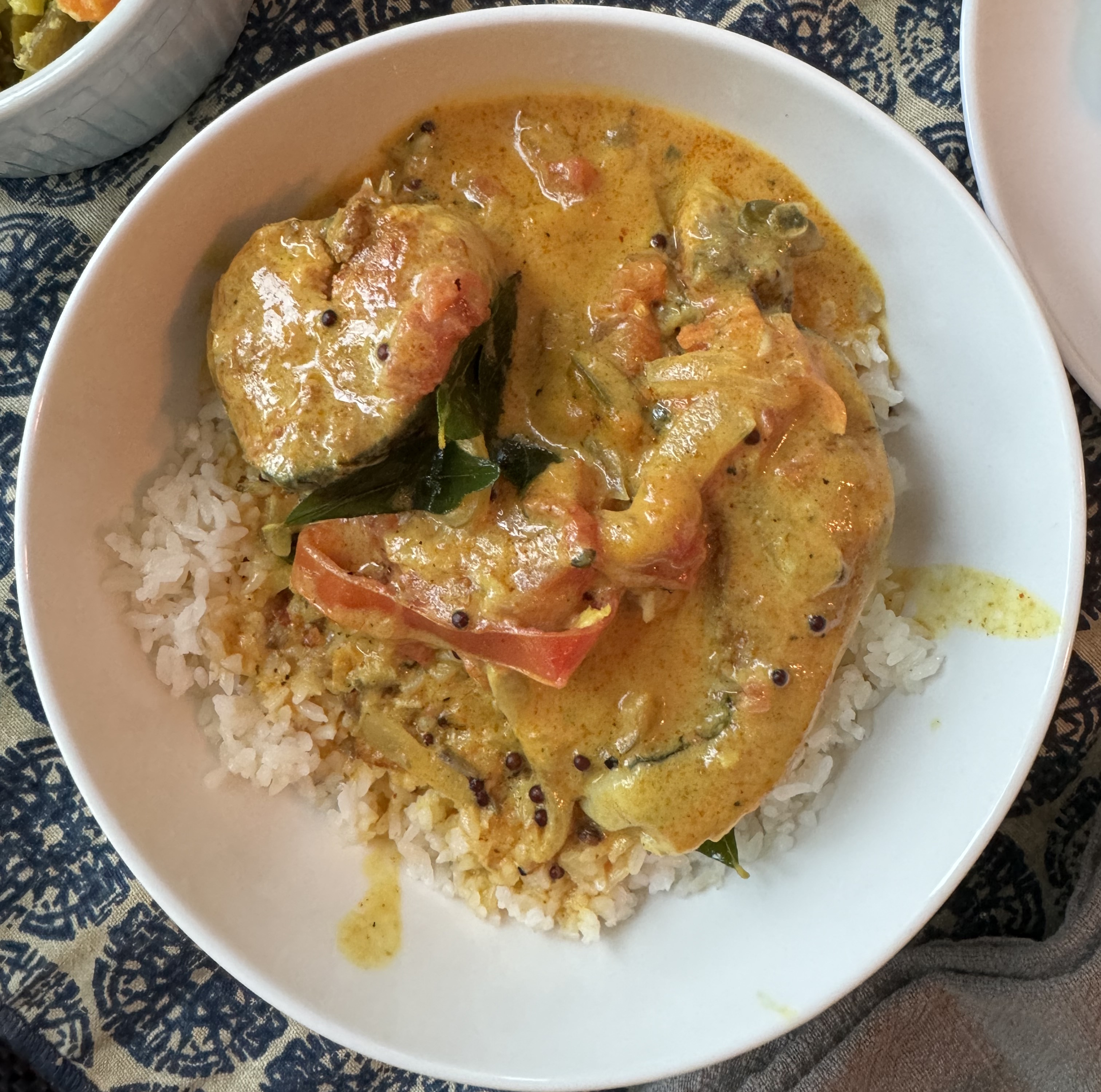 Bowl of rice with a fish curry on top. There are two huge chunks of fish, sliced as steaks off a whole fish. The curry is vibrant orange. Some vegetables and curry leaves are visible in the sauce.