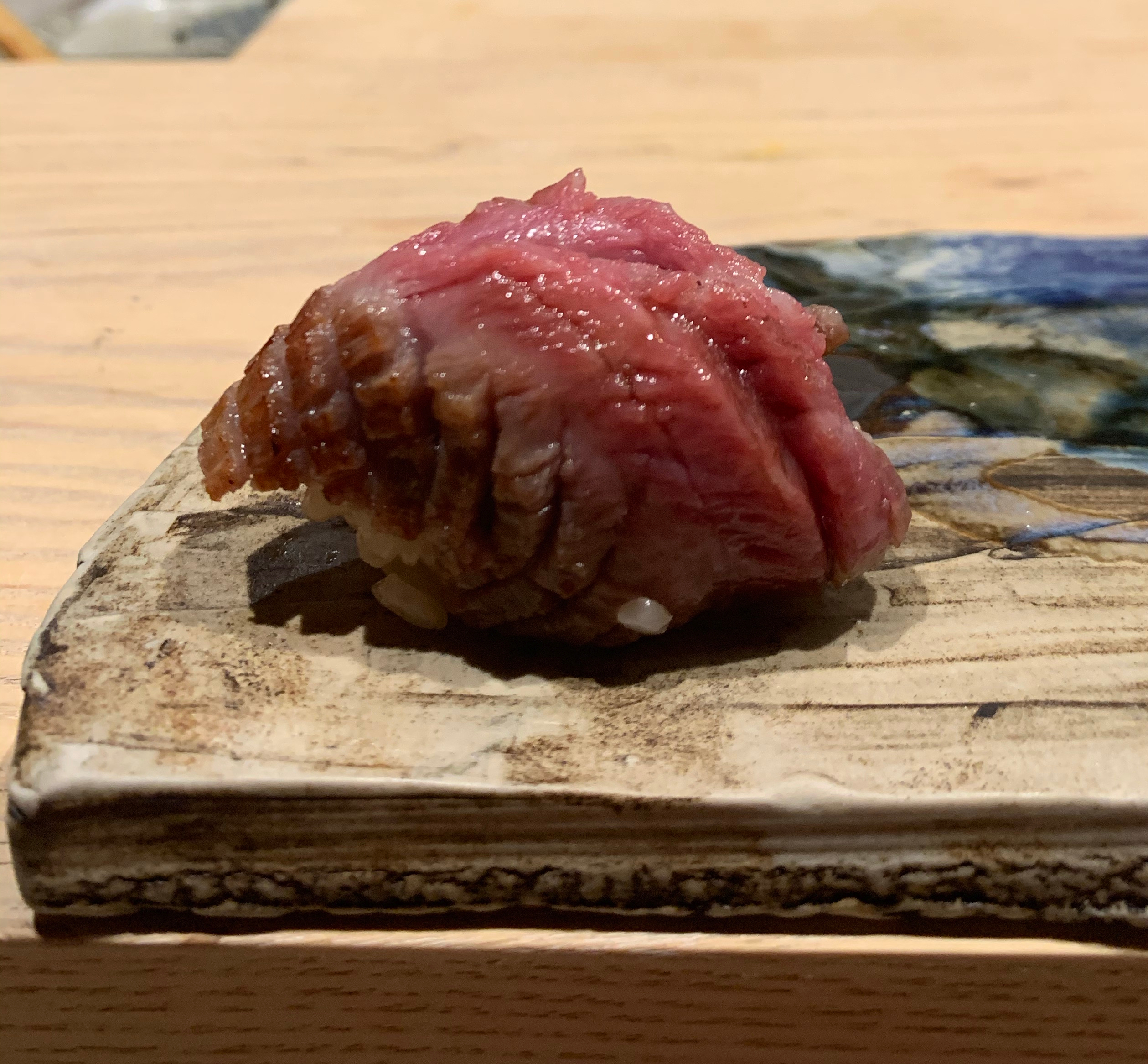 One piece of nigiri sushi with seared beef on top. The beef is golden brown along the side, but in the middle the rare flesh is exposed. 