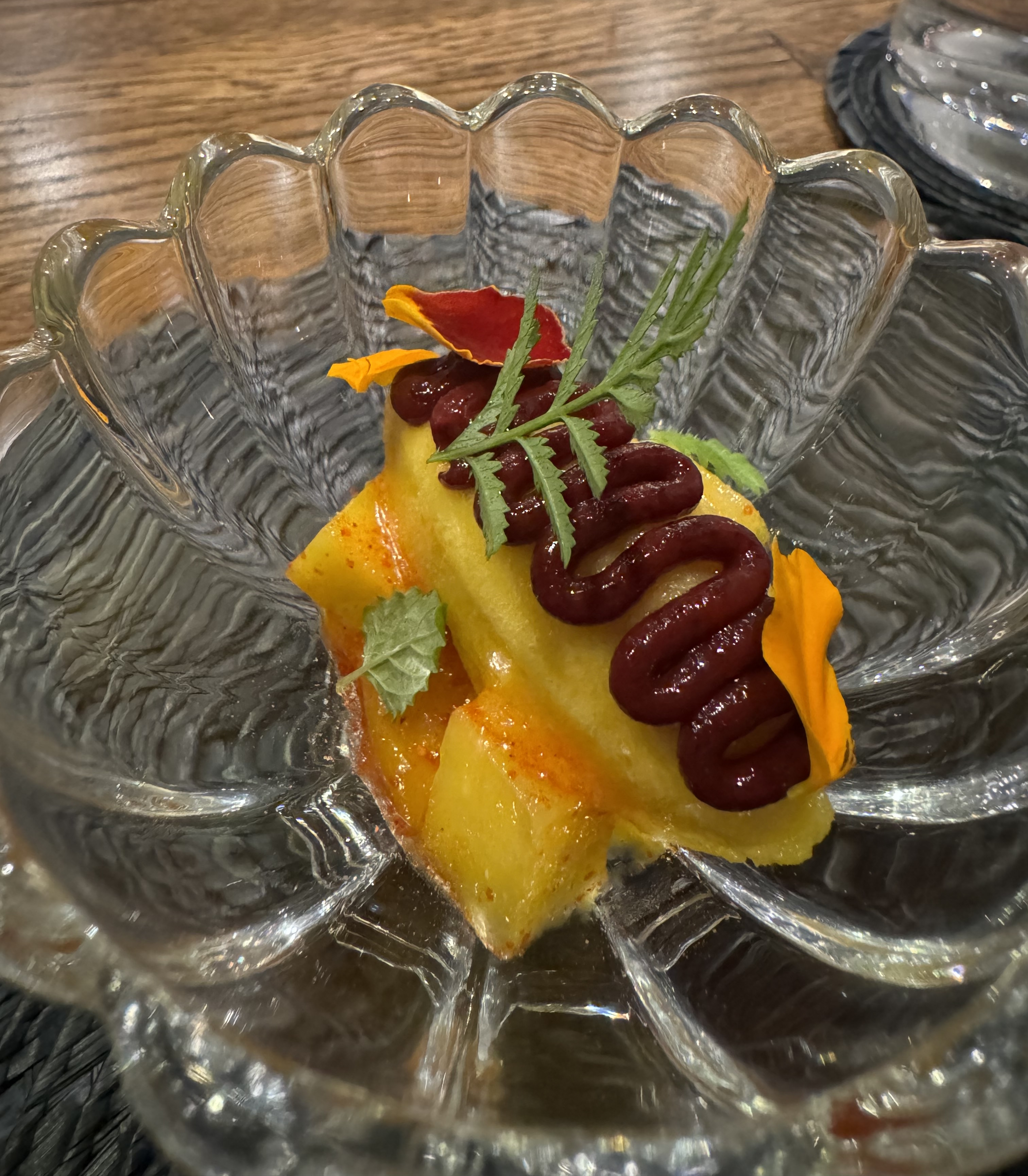 Quenelle of orange sorbet sitting on top of a few mango cubes. There's a squiggle of dark red sauce on top of the quennelle, and a few tiny green leaves for garnish.