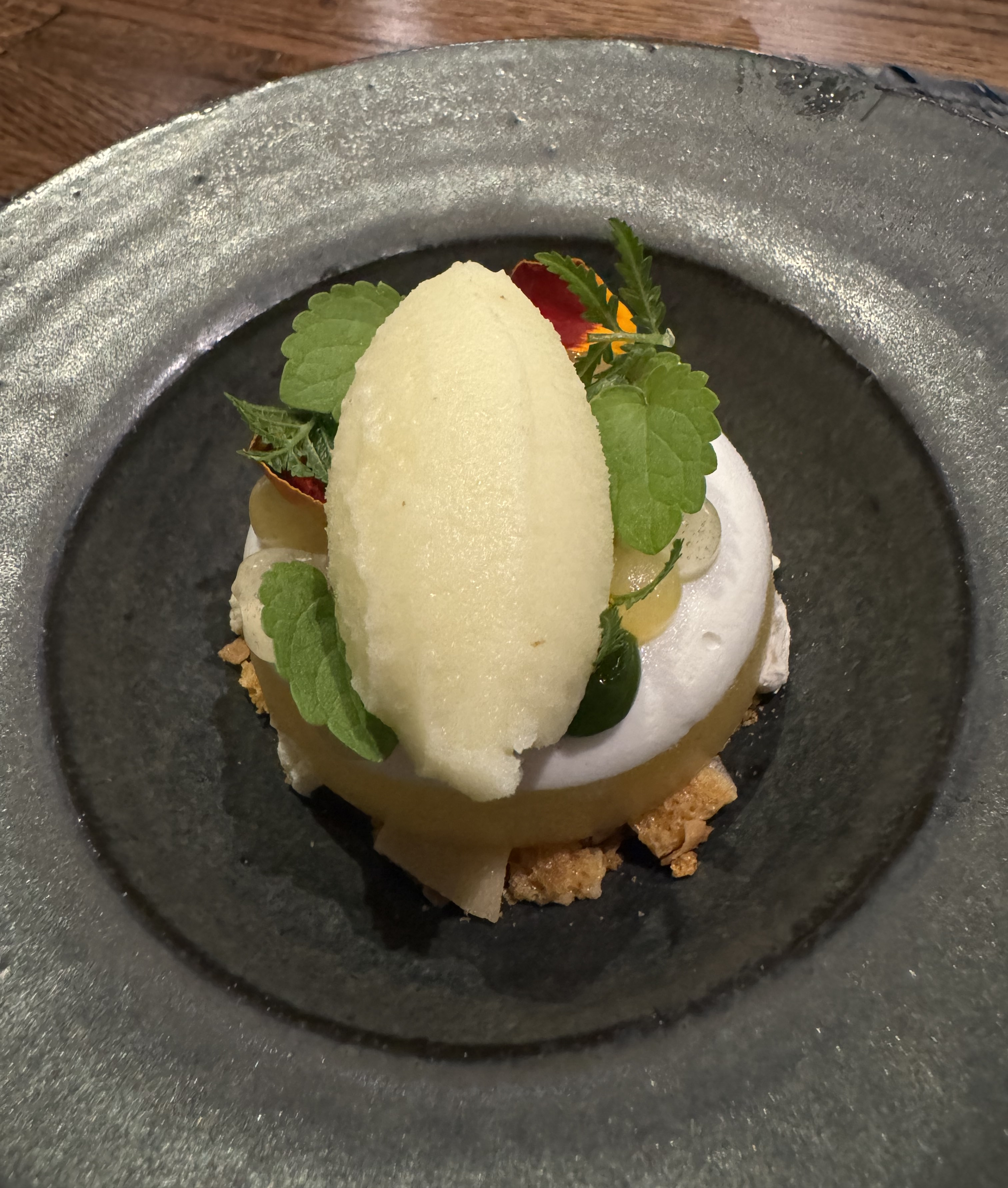 Ring of yellow gel topped with a white frosting. There are some dots of sauce on top of the frosting, obscured by a quennelle of ice cream. There is a crumble beneath the ring, barely visible.