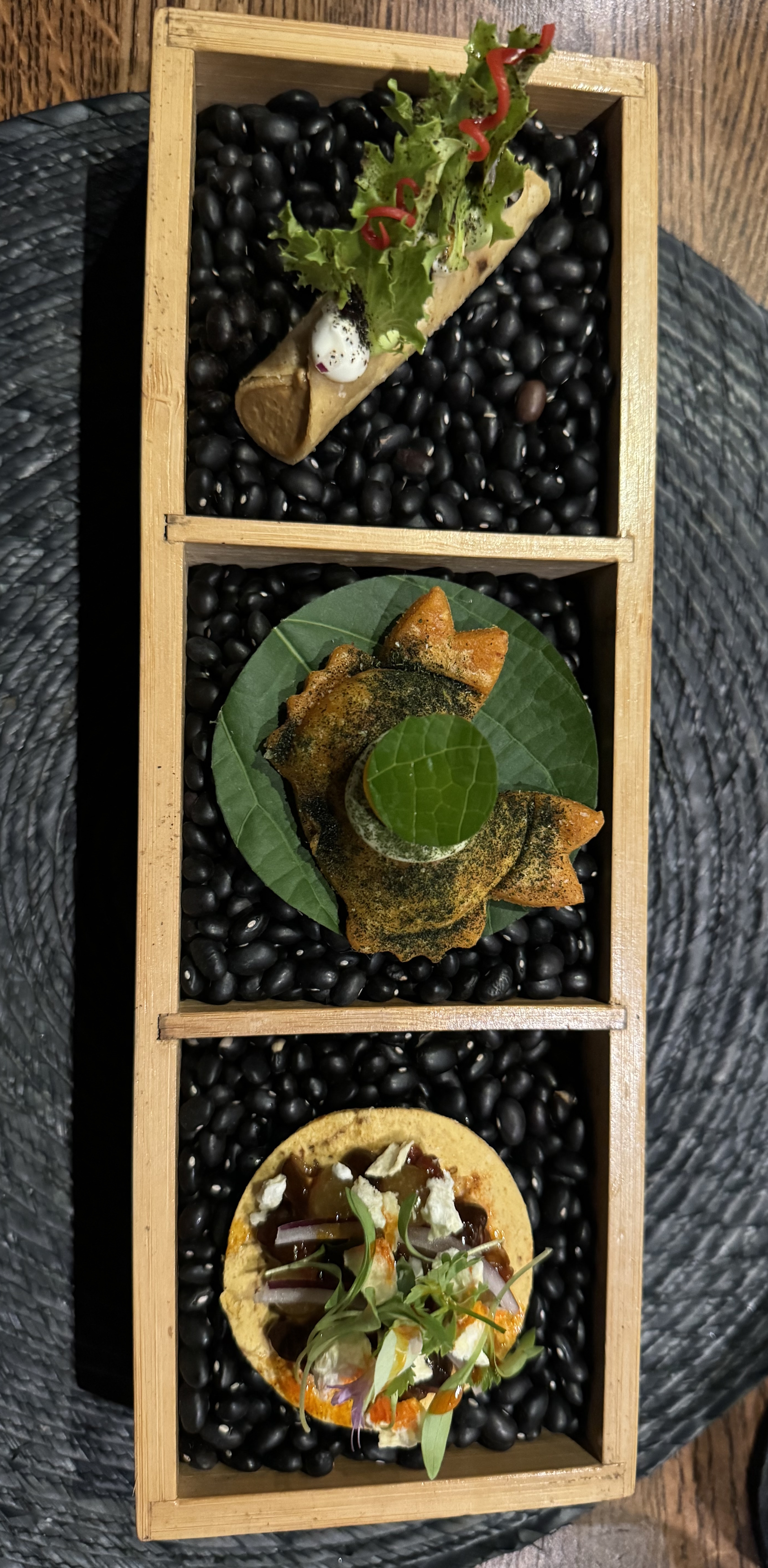 A box with three compartments full of dried beans. Each pile of beans has one- or two-bite taco or empenada.