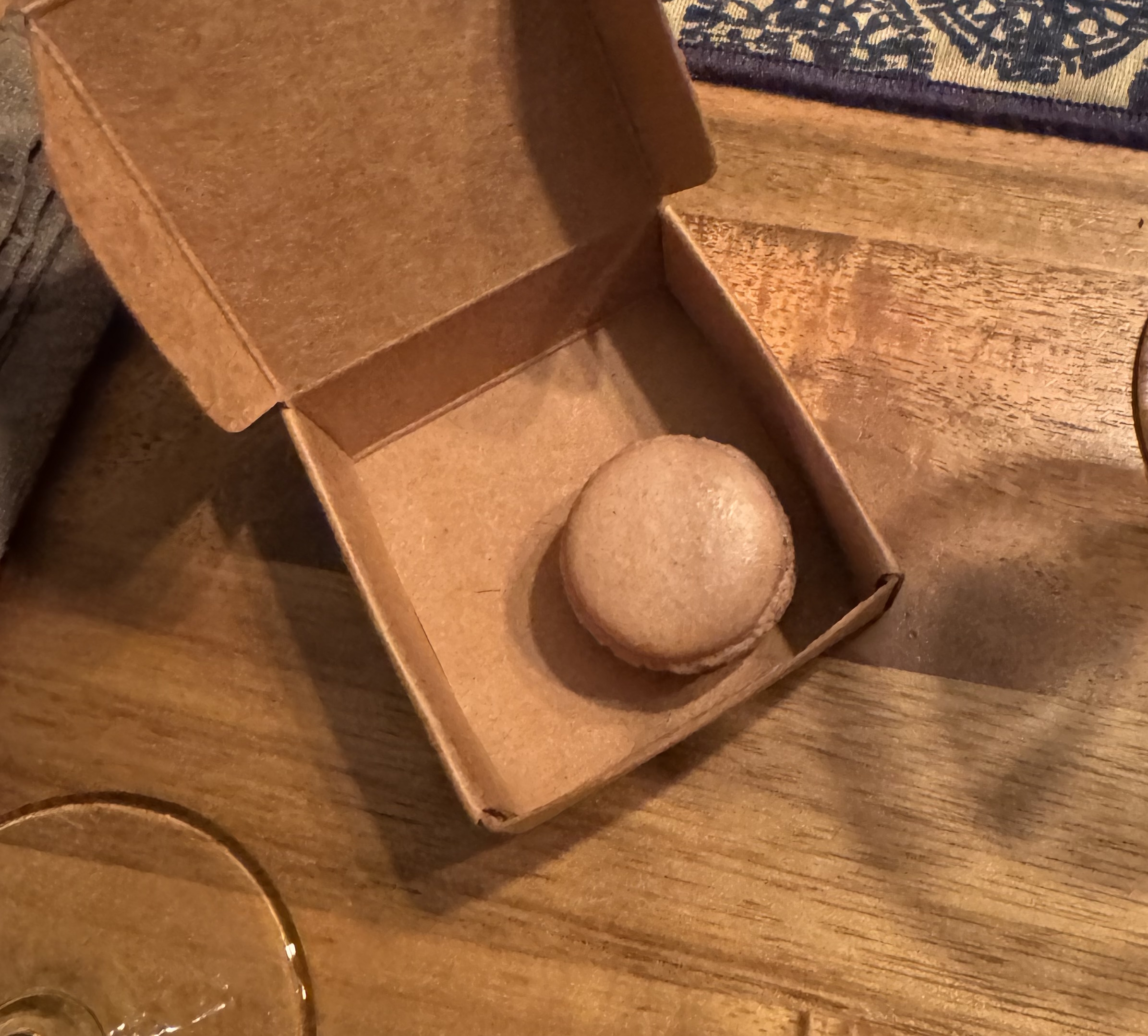 Small cardboard box with a single light-brown macaron inside.