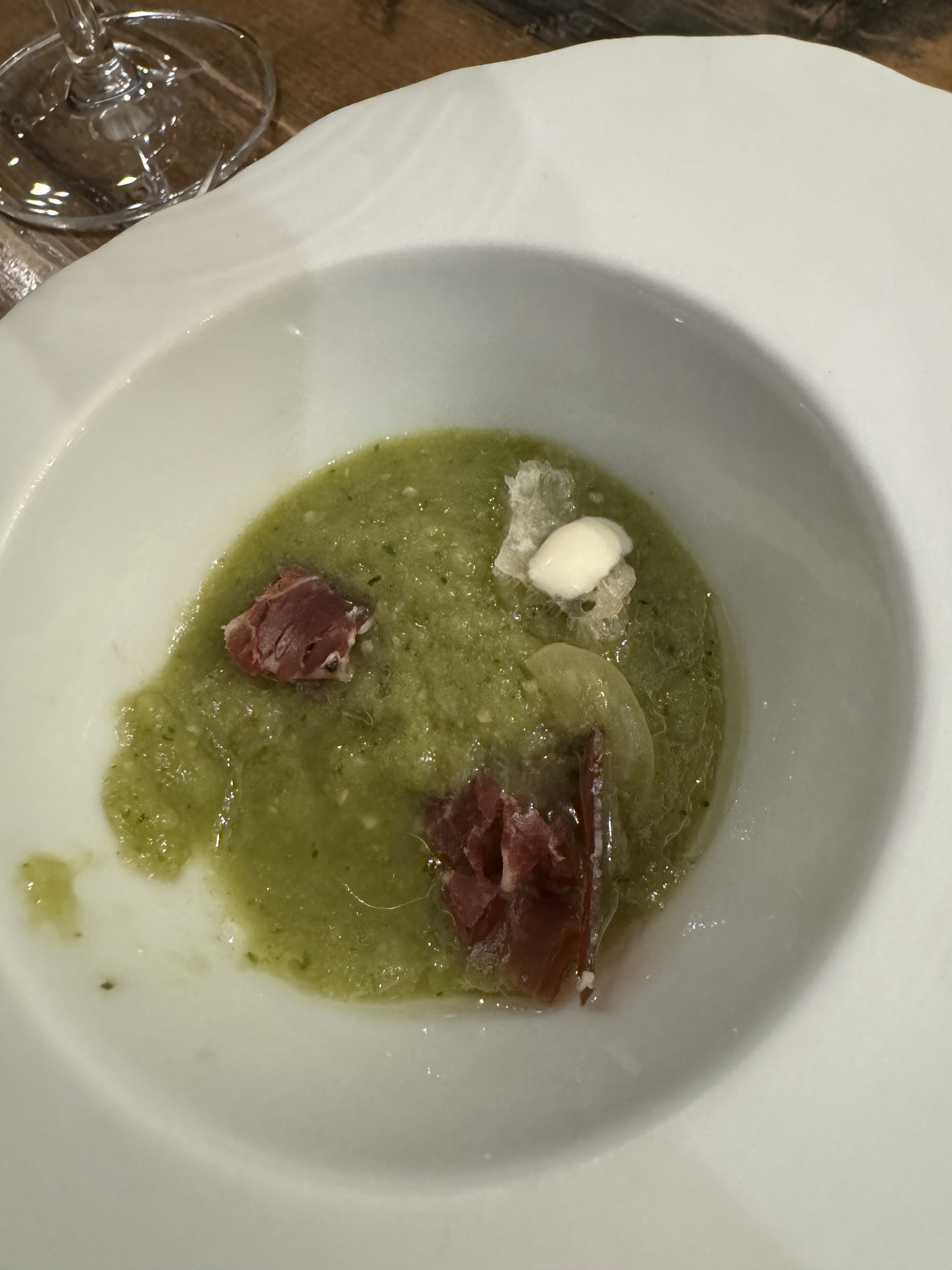 Bowl of a thick green soup, garnished with some super-thin-sliced bits of dark red ham and a few crumbles of fresh cheese