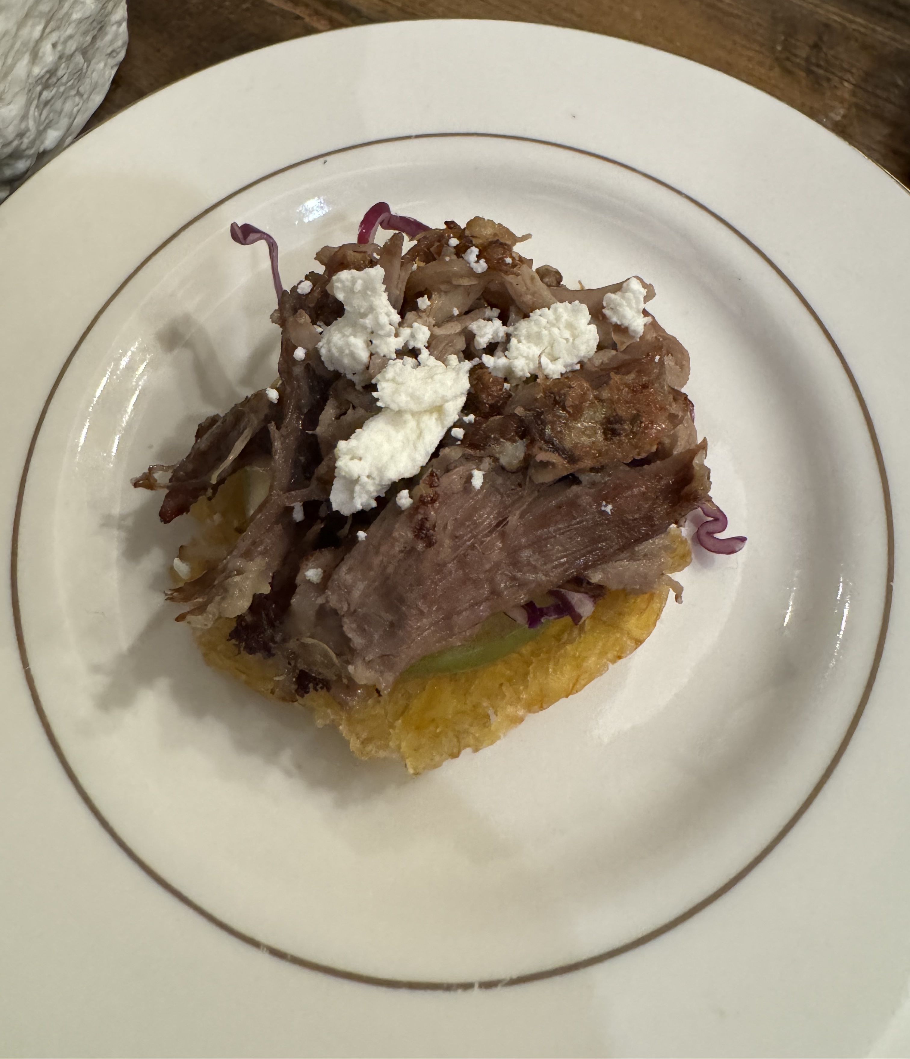 Roasted pork with some fresh cheese on top of a slice of something green, sitting atop a pale yellow plantain shell