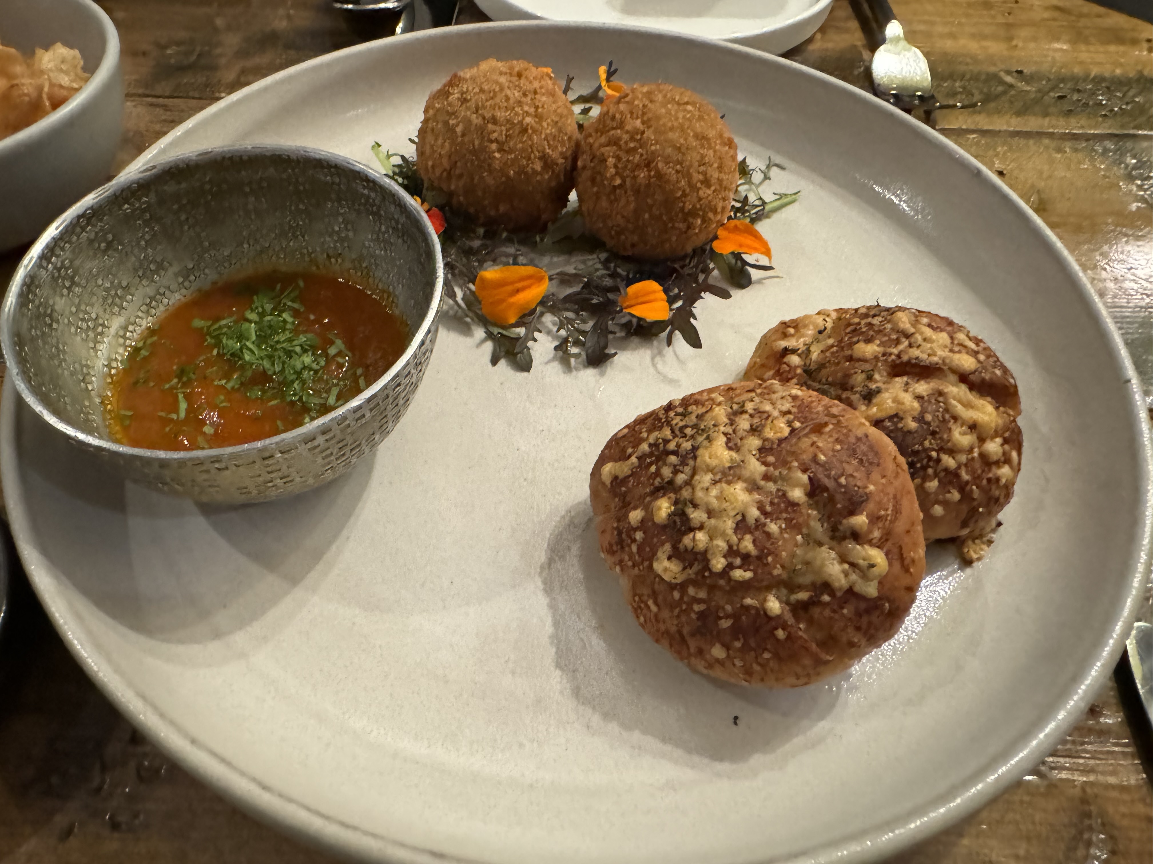 Plate with a bowl filled with a thick red tomato sauce, two rolls encrusted with parmesan cheese, and two fried balls.