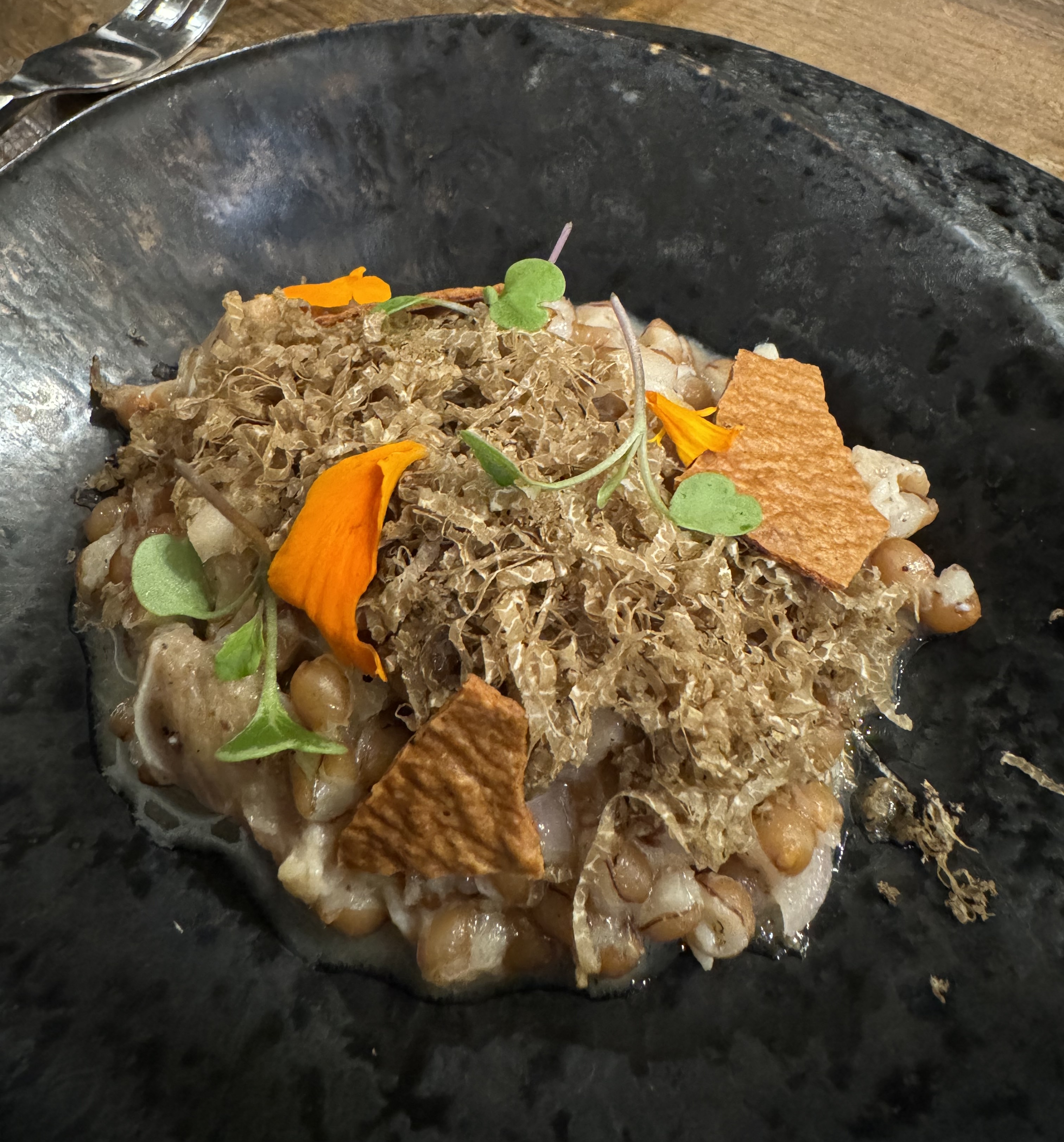 Heap of wheat berry porridge garnished with light-brown shavings of truffle and some shards of a yellow cracker