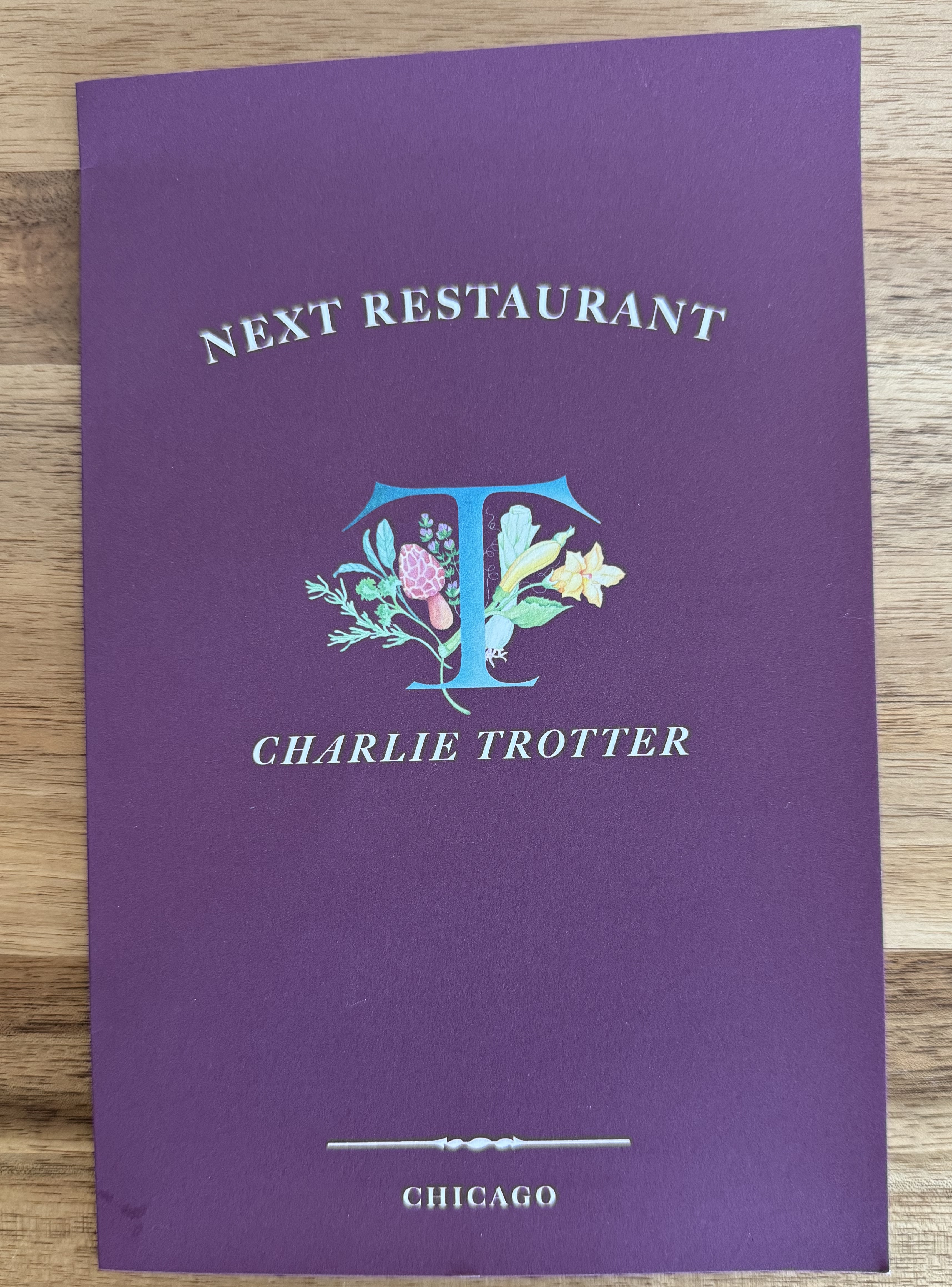 Purple book that says Next Resutrant, Charlie Trotter. It has the Trotter's logo, a blue T with flowers behind it.