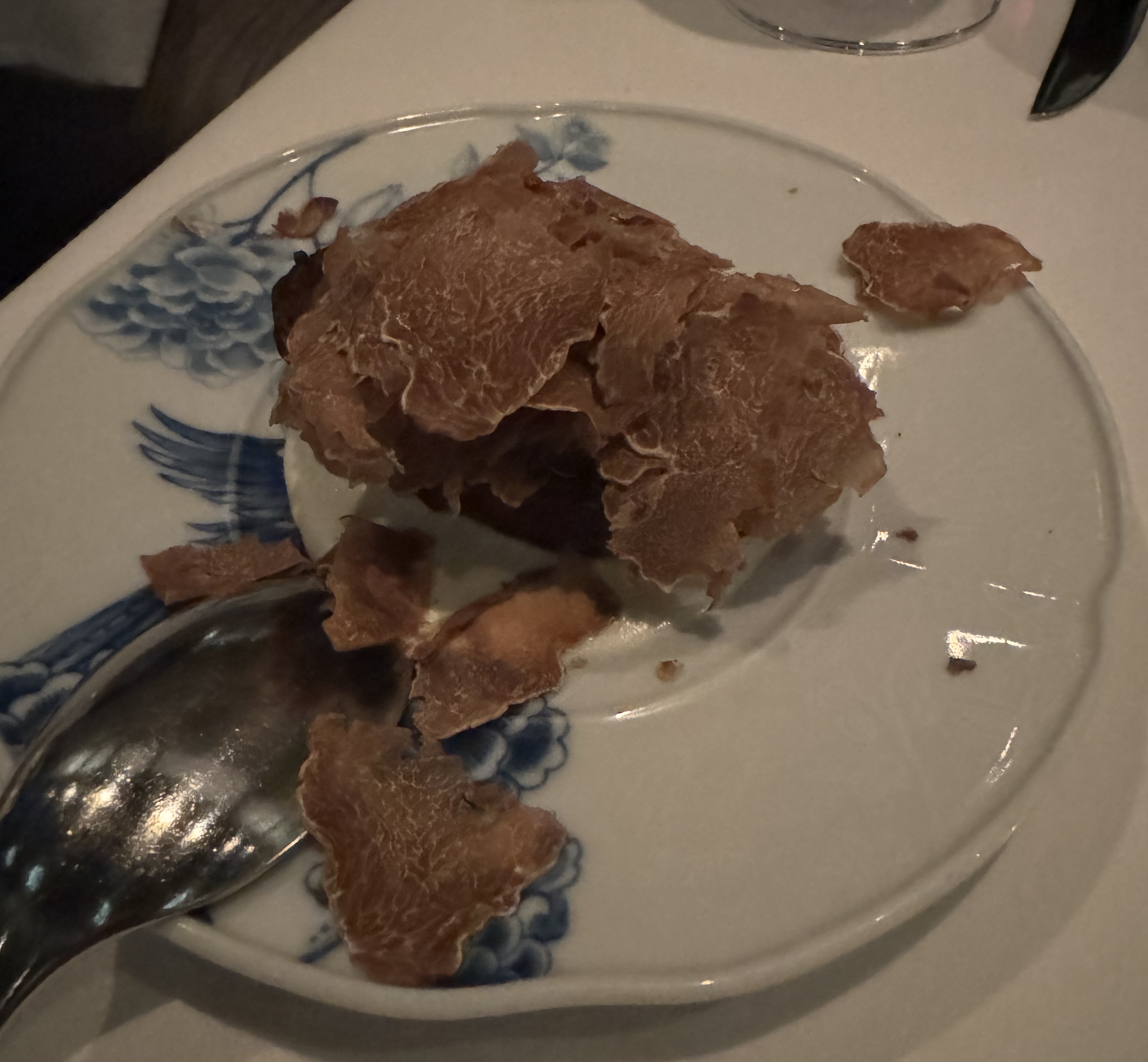 Small plate with something on it. The "something" is obscured by shaved white truffle. The white truffle is a huge heap and has spilled onto the plate.