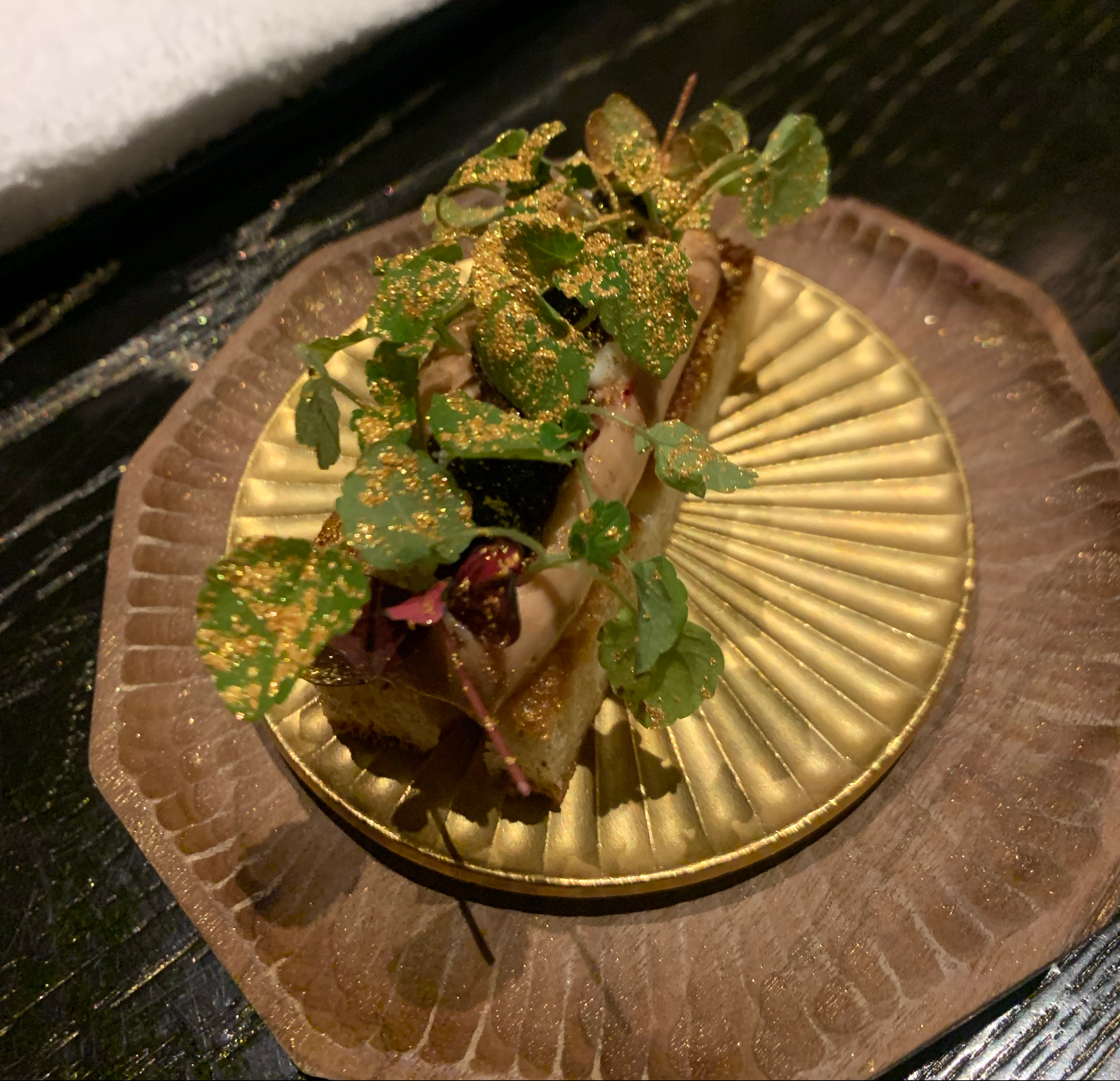 Toast topped with mouse, microgreens, and tons of gold dust on a golden plate