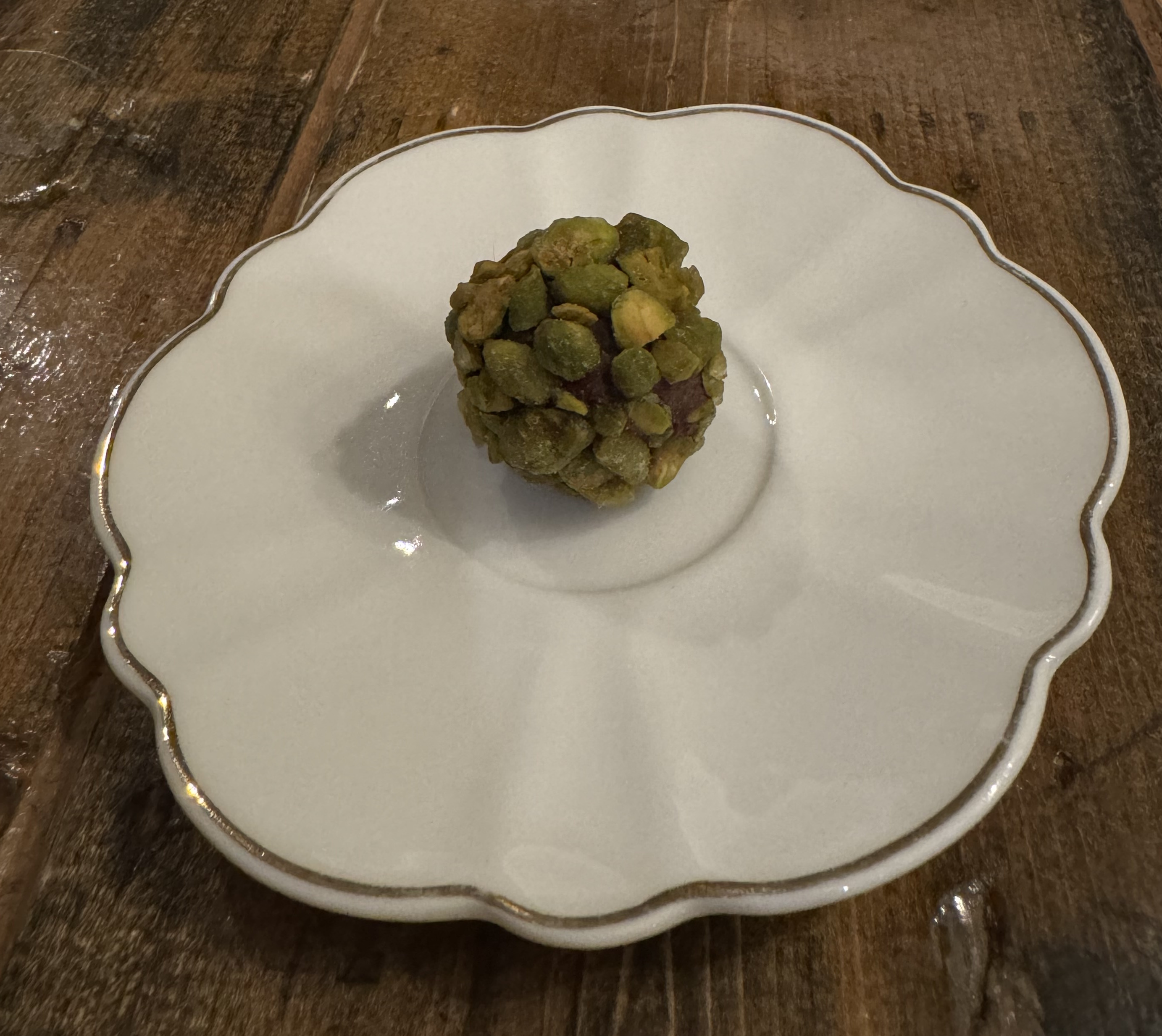 Tea saucer with a single item in the center: a chocolate ball studded with halved pistachio nuts.