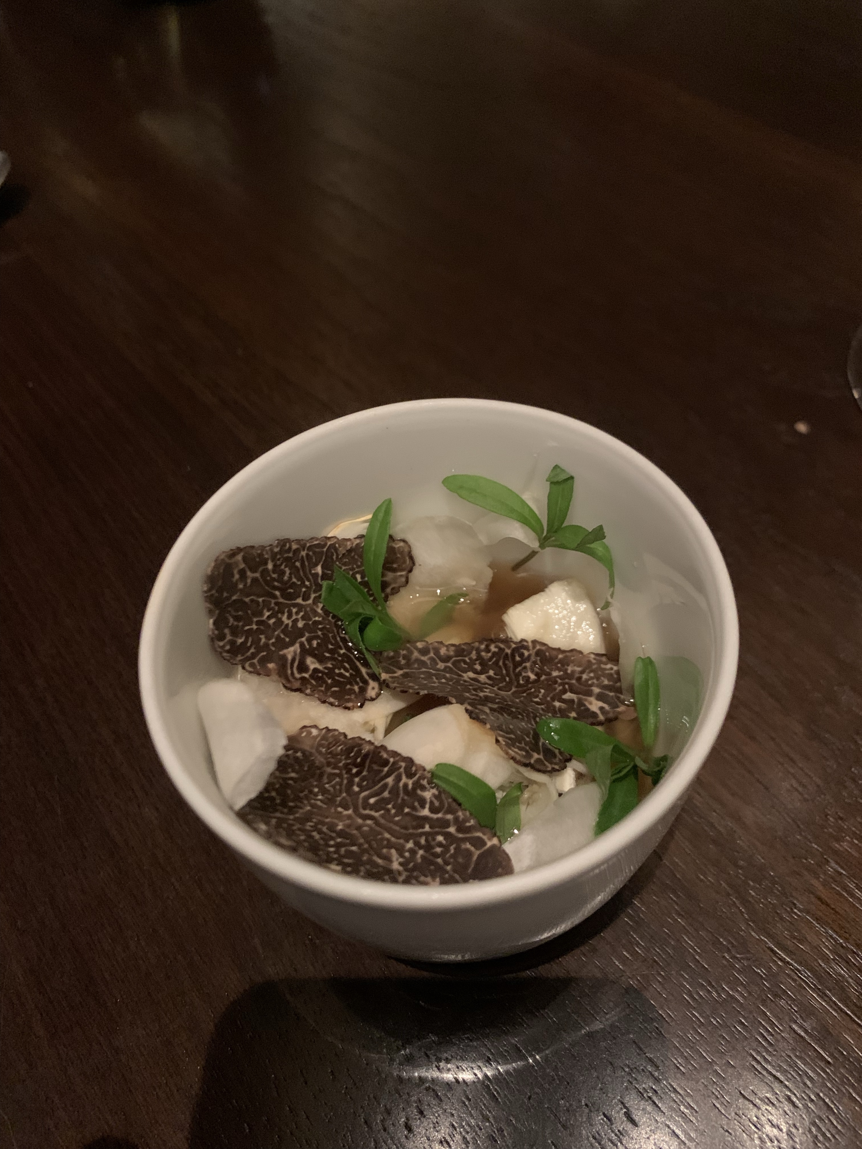 Shaved black truffle in a bowl topping custard cubes, with a broth in the bottom of the bowl