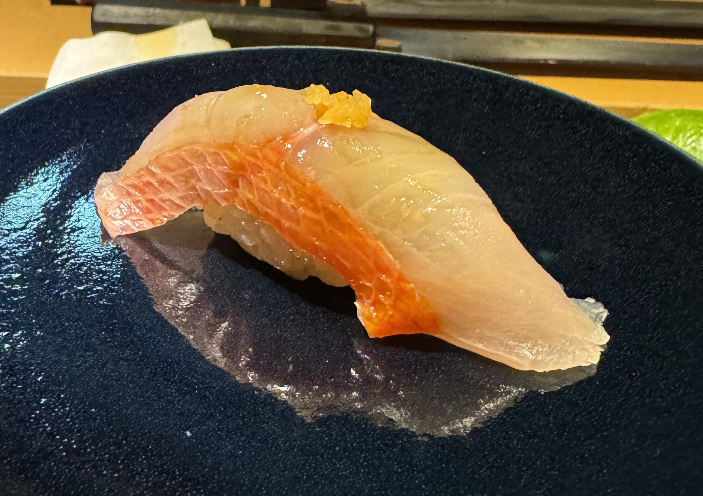 A light white fish on top of rice. The fish has a band of pink skin with white cross-hatching on the side. There is a small pile of yellow specks on top as garnish