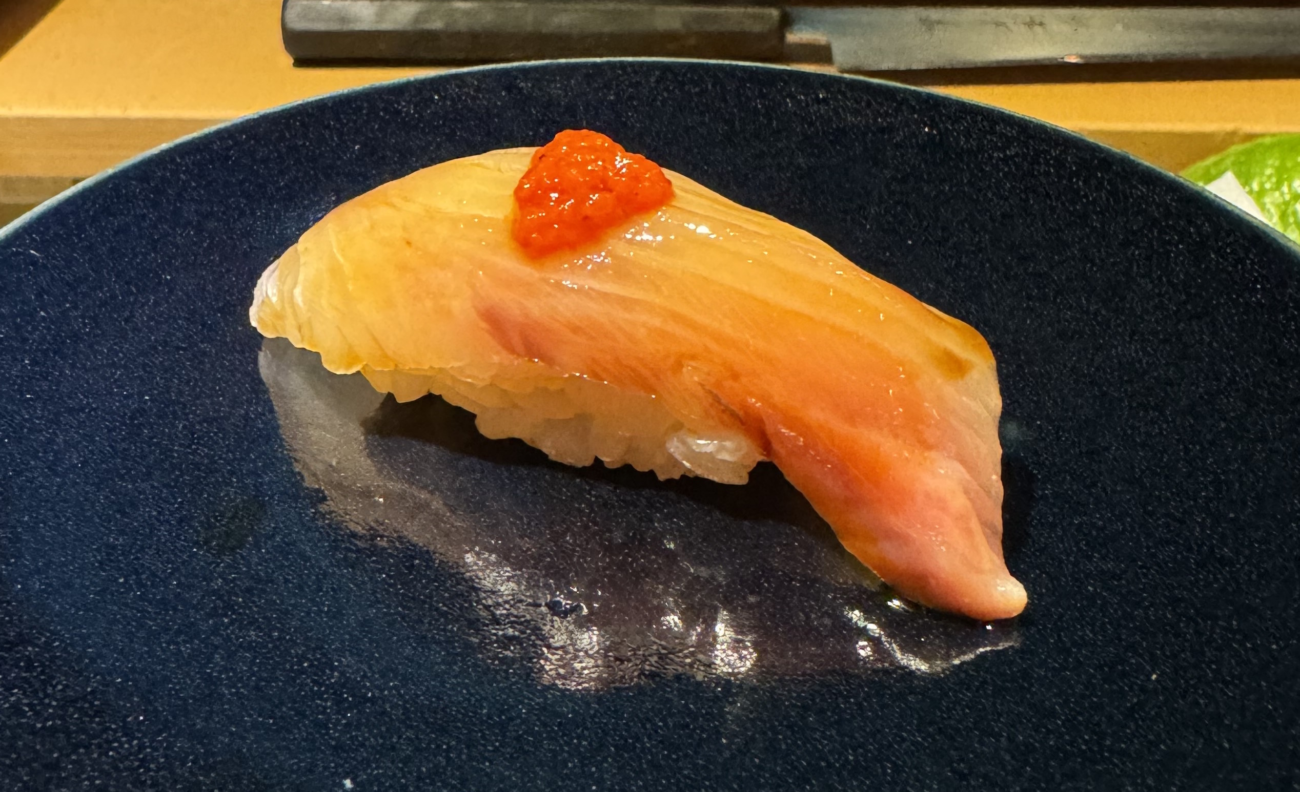 A slightly yellow fish on top of rice. Towards the back, there is a band of red-pink flesh. It's glistening from a light brushing of oil or dark sauce. There is a dollop of a red sauce on top.