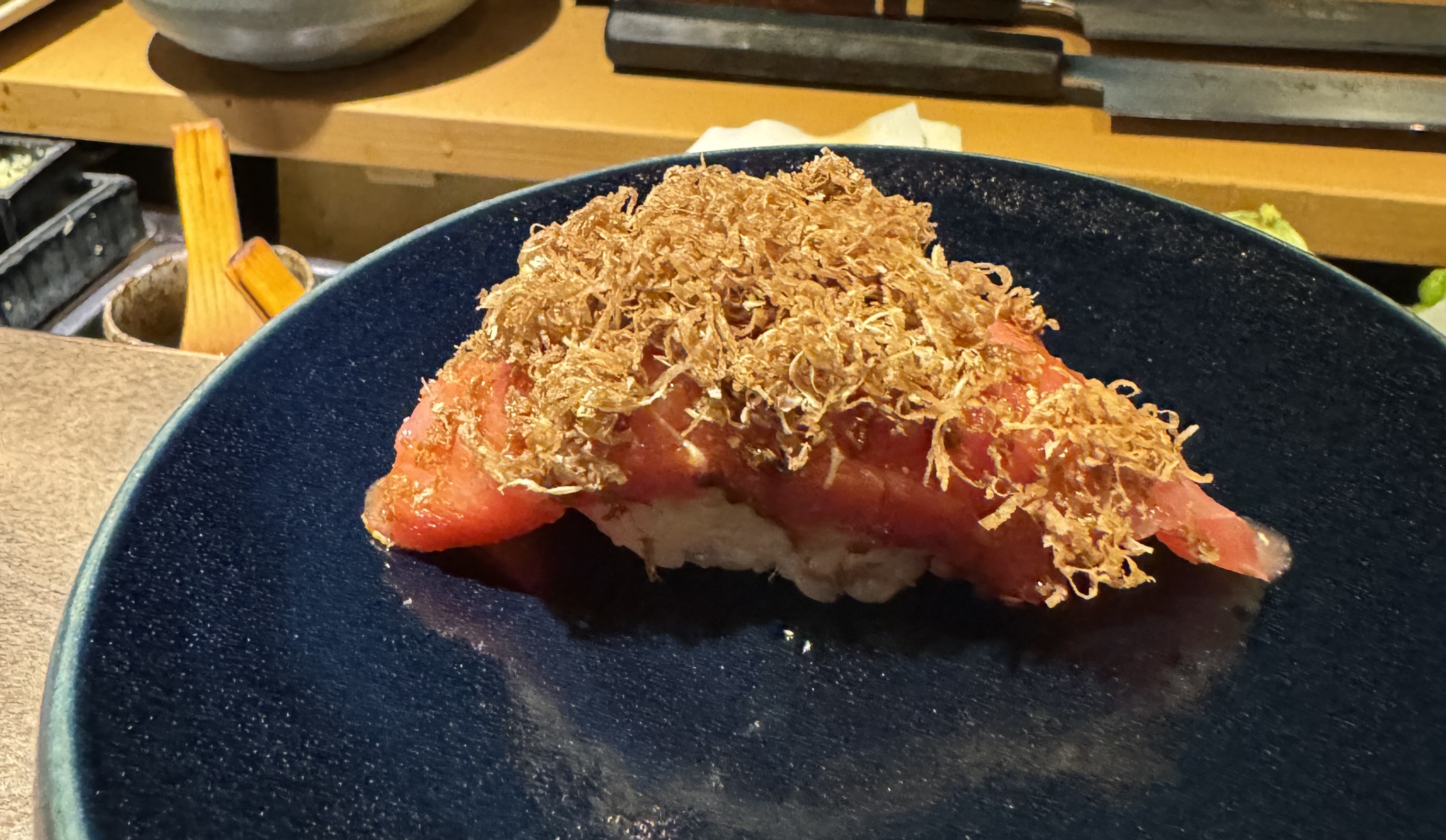 A piece of red fish, slightly less bright-red than the lean tuna, sitting on top of rice. The fish has been sprinkled with shreds of a light-brown, fluffy substance: truffle. It's heaped generously with the grated truffle.