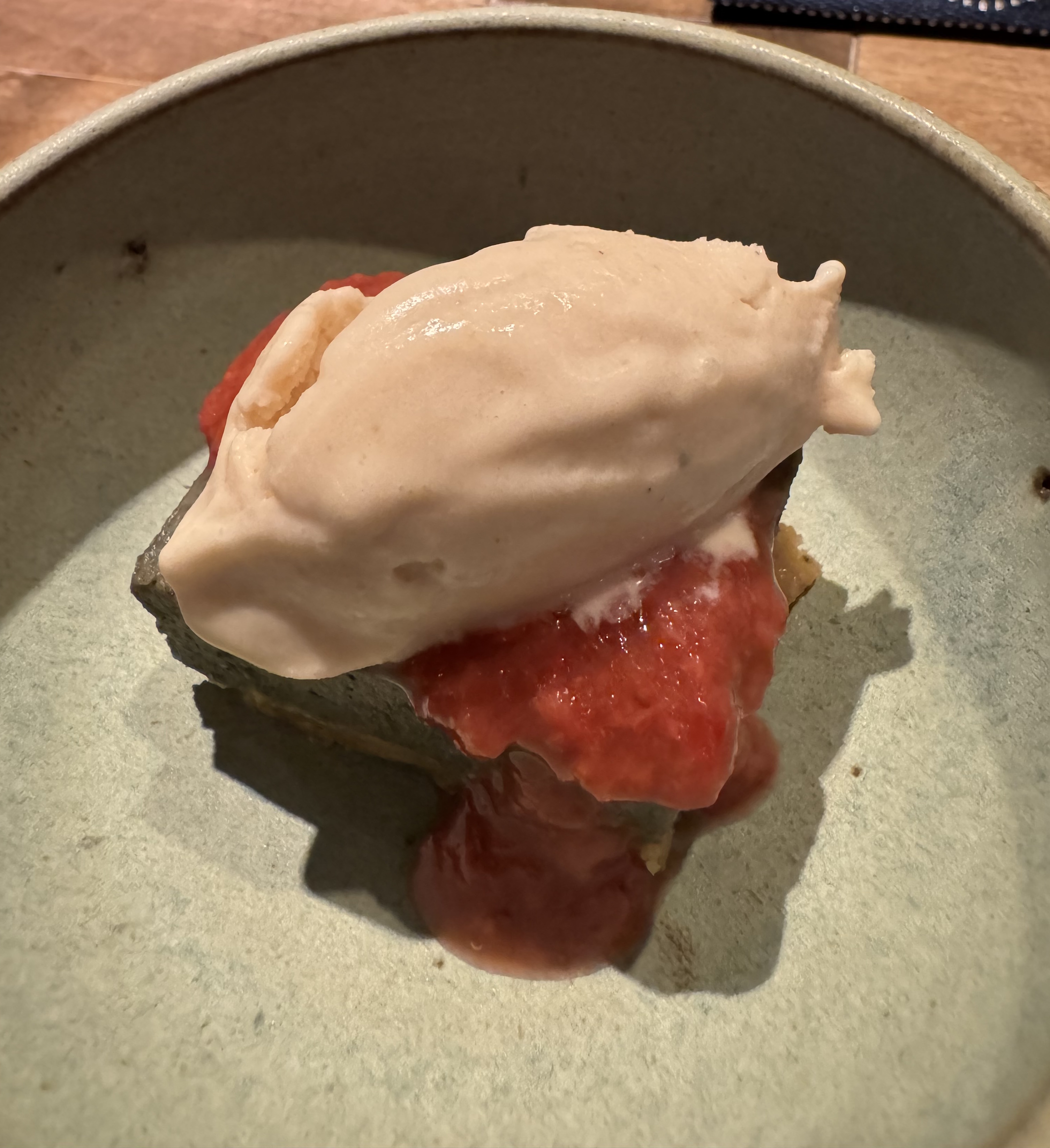 A black square of cake topped with a thick red sauce and a quenelle of pink ice cream. The sauce has some tiny-but-visible chunks, and has cascaded down one corner of the cake.