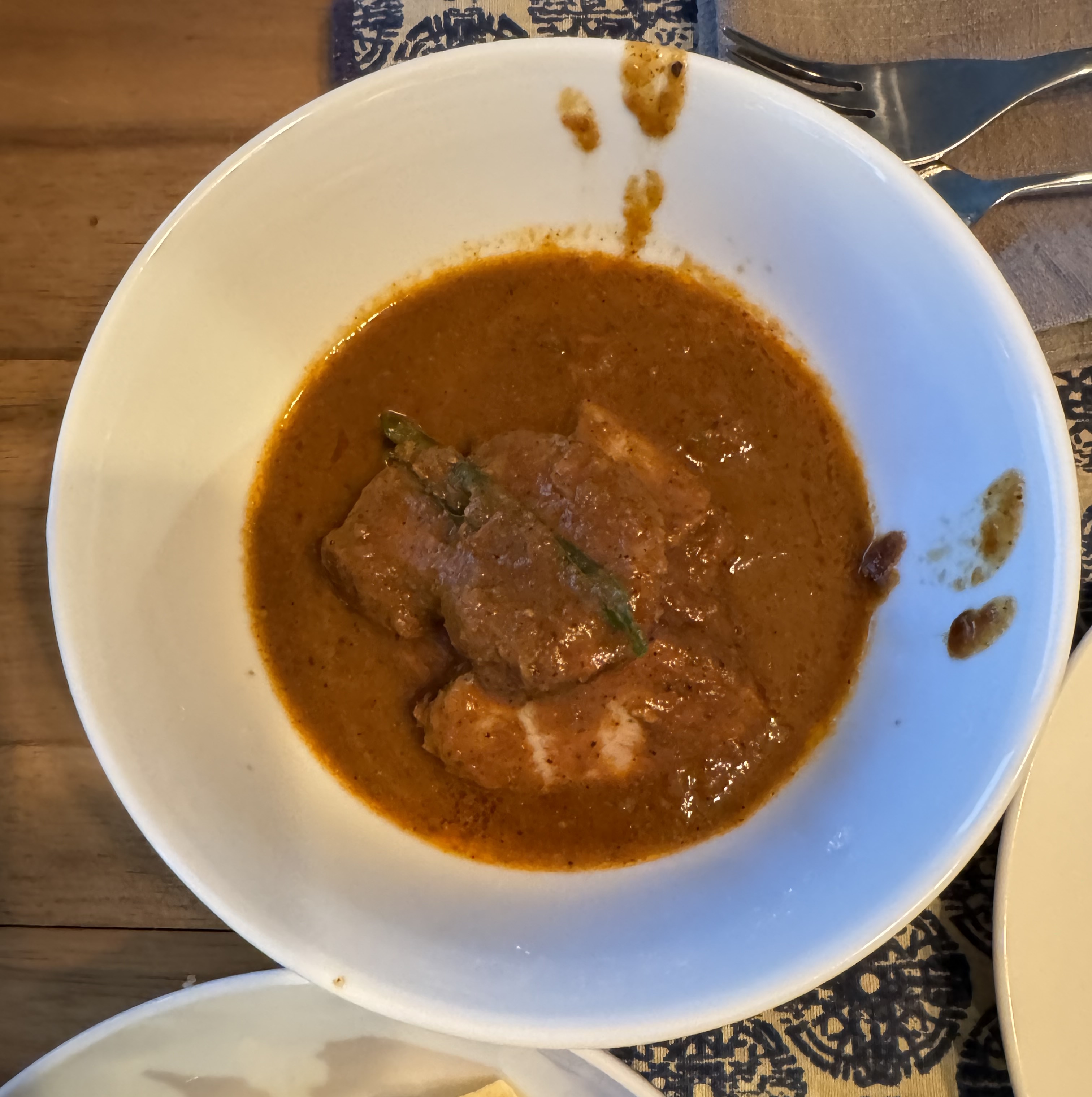 Thick slices of duck breast in a brown gravy, with a single curry leave barely visible under the surface of the gravy.