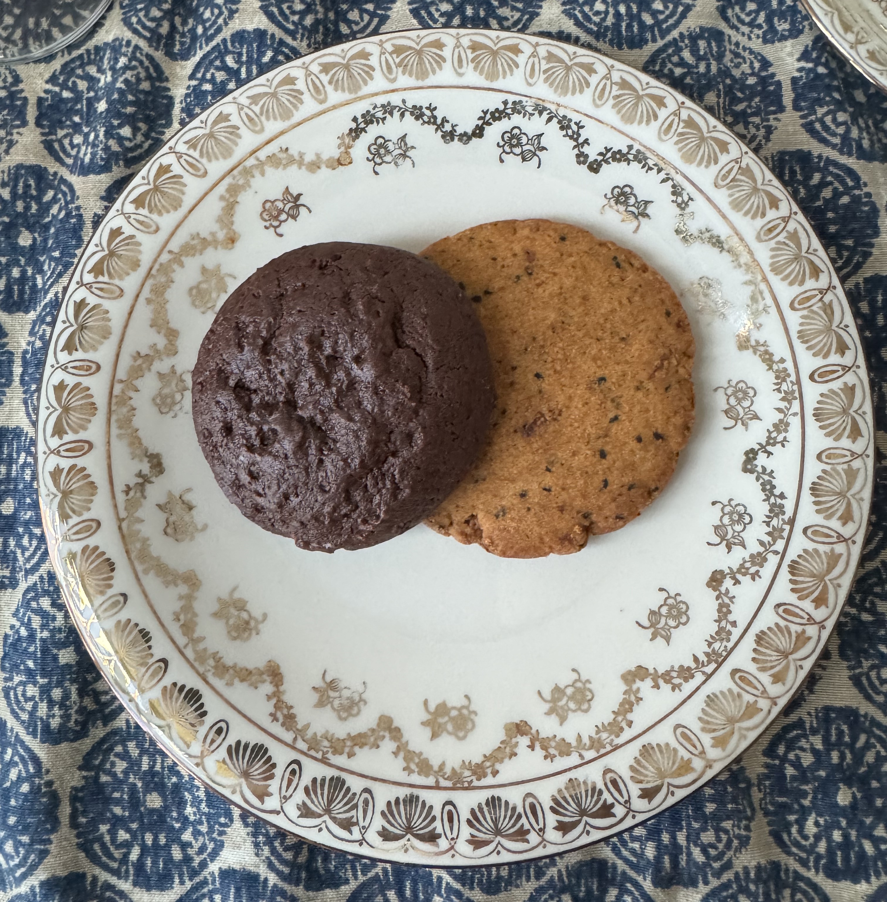 Two cookies on a fancy plate. There is a chocolate cookie, and a light brown cookie with specks of black.