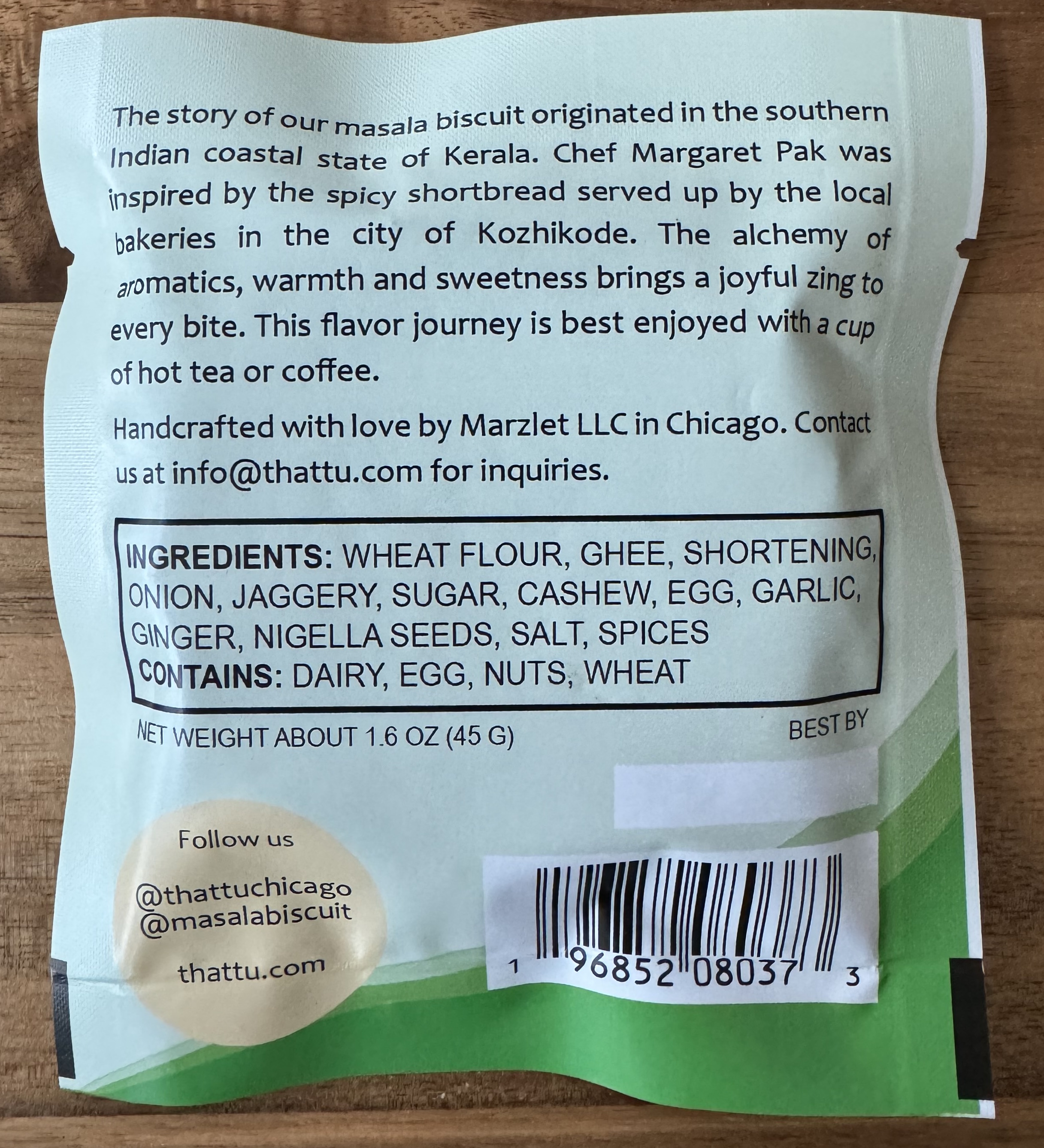 The back of a packaged cookie. 

The story of our masala biscuit originated in the southern Indian coastal state of Kerala. Chef Margaret Pak was inspired by the spicy shortbreads served up byt he local bakaries in the city of Kozhikode. The alchemy of aromatics, warmth and sweetness brings a joyful zing to every bite. The flavour journey is best enjoyed with a cup of hot tea or coffee.

Handcrafted with lvoe by Marzlet LLC in Chicago. Contact us at info@thattu.com for inquiries. 

Ingredients: Wheat flour, ghee, shortening, onion, jaggery, sugar, cashew, egg, garlic, ginger, nigella seeds, salt, spices.  CONTAINS: DAIRY, EGG, NUTS, WHEAT.

Net weight: about 1.6 oz (45g).