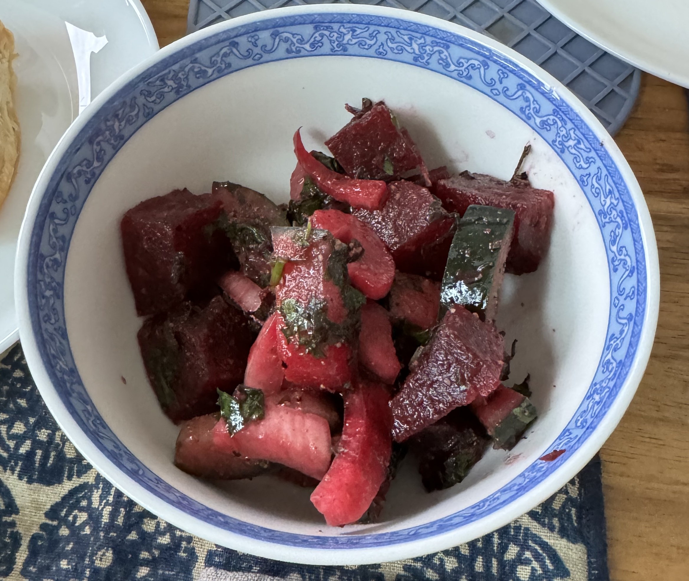 Small bowl of sliced beets, and other vegetables that have taken on a red hue thanks to their proximity to the beet. A slice of cucumber is visible because it's skin has not been dyed red, yet.