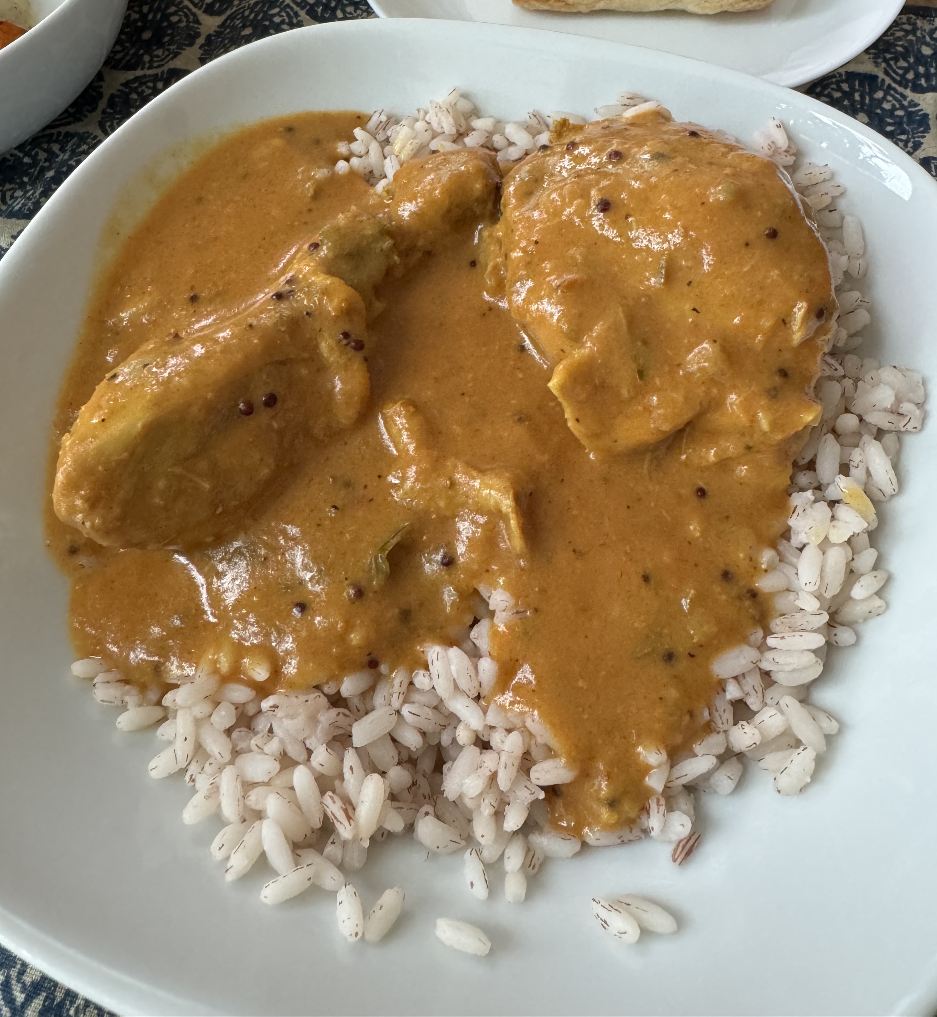 A bowl of off-white rice with a slight redish-purple hue. There is an orange-brown sauce over the rice, with specks of black spices in it. A chicken thigh & drumstick are visible, coated in the sauce. 