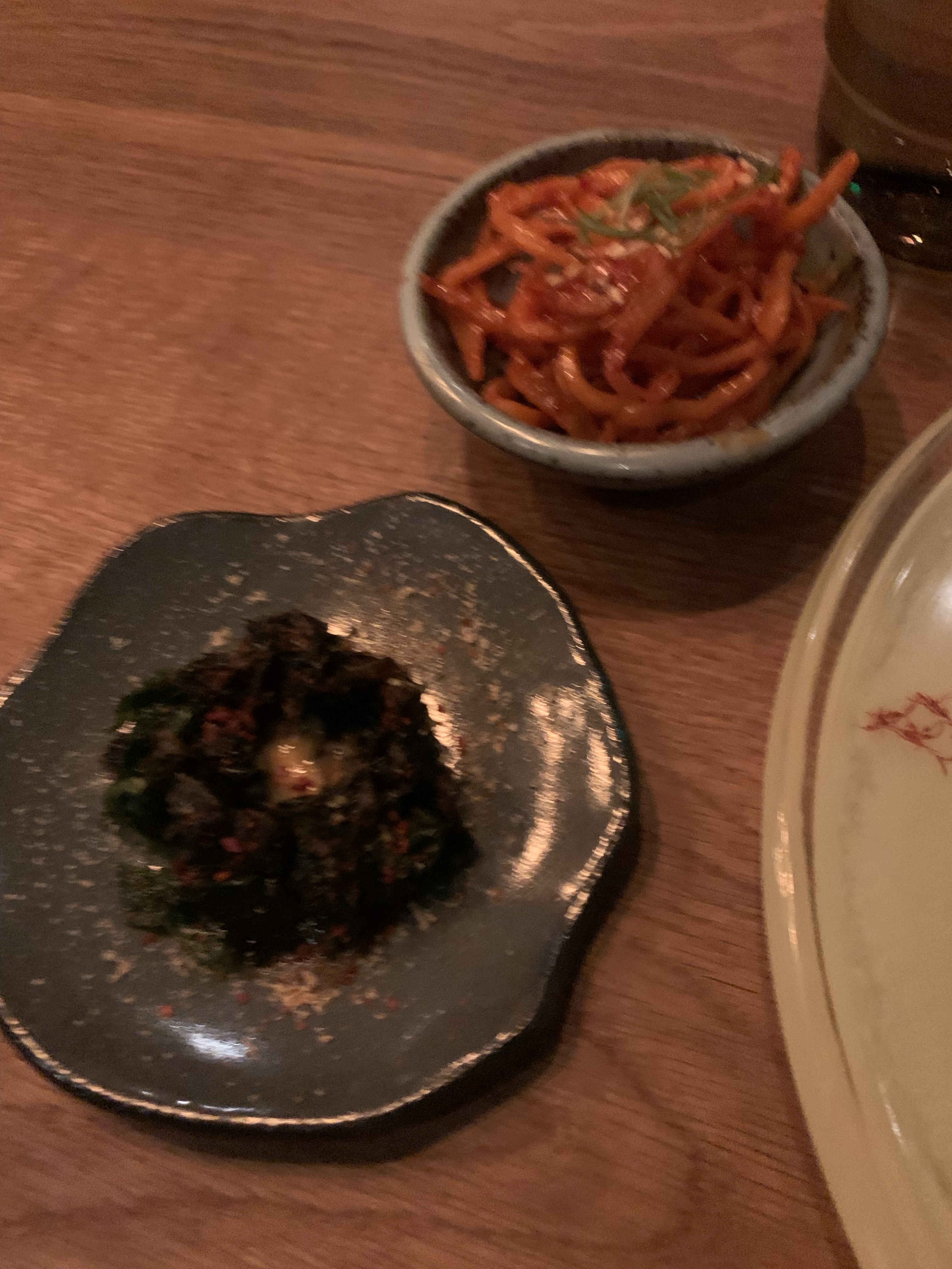 A plate of black sea vegetables, and a plate of bright-red spicy noodle-looking things