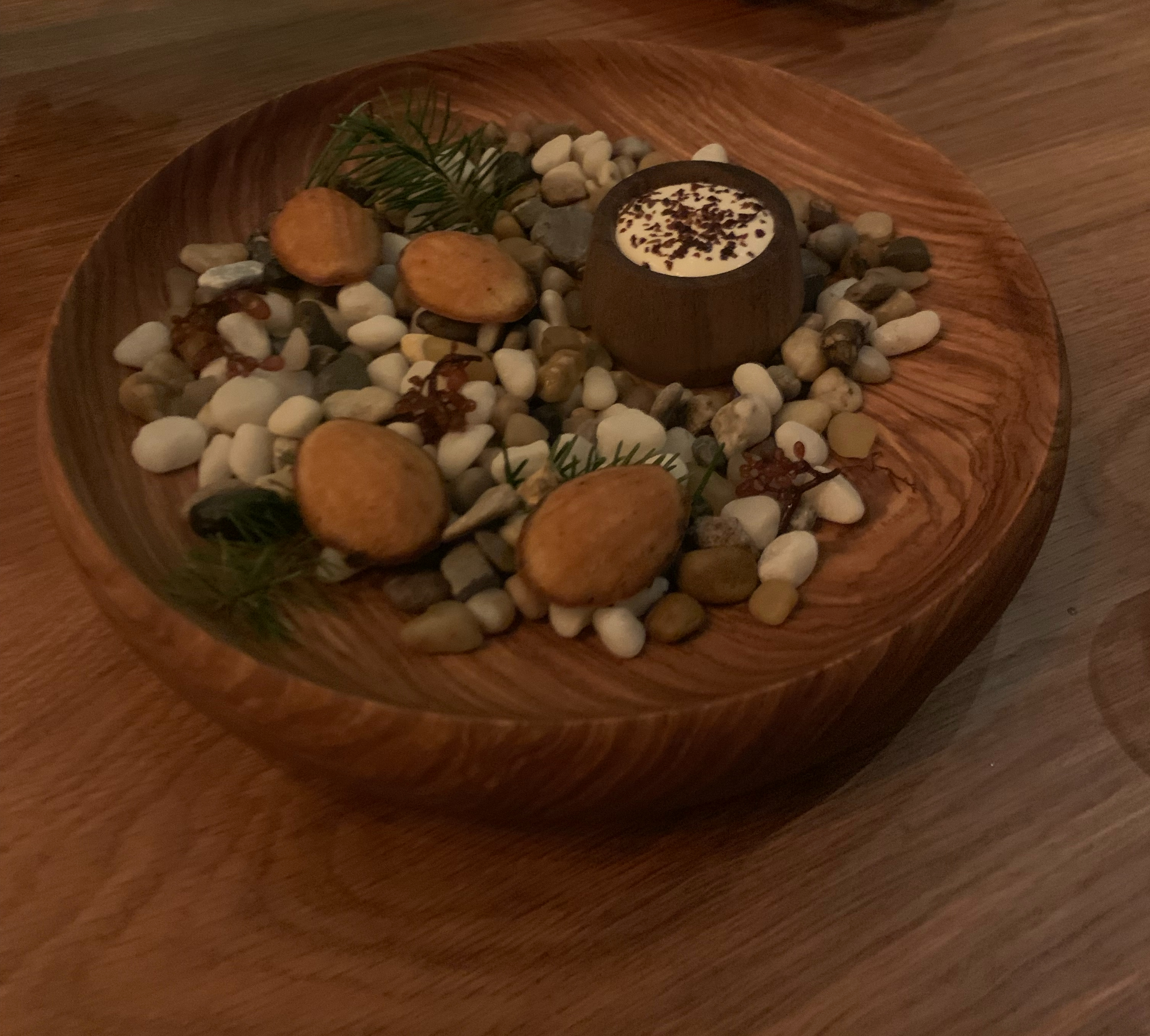 Four madeline cookies served atop a bed of rocks collected at the beach, with a pot of creme fresh for dipping next to them