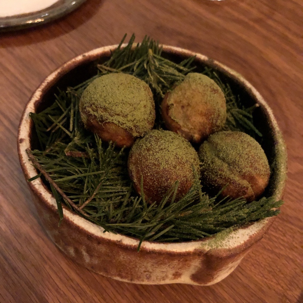 Four golden-brown balls served on a bed of pines, with a dusting of a green powder