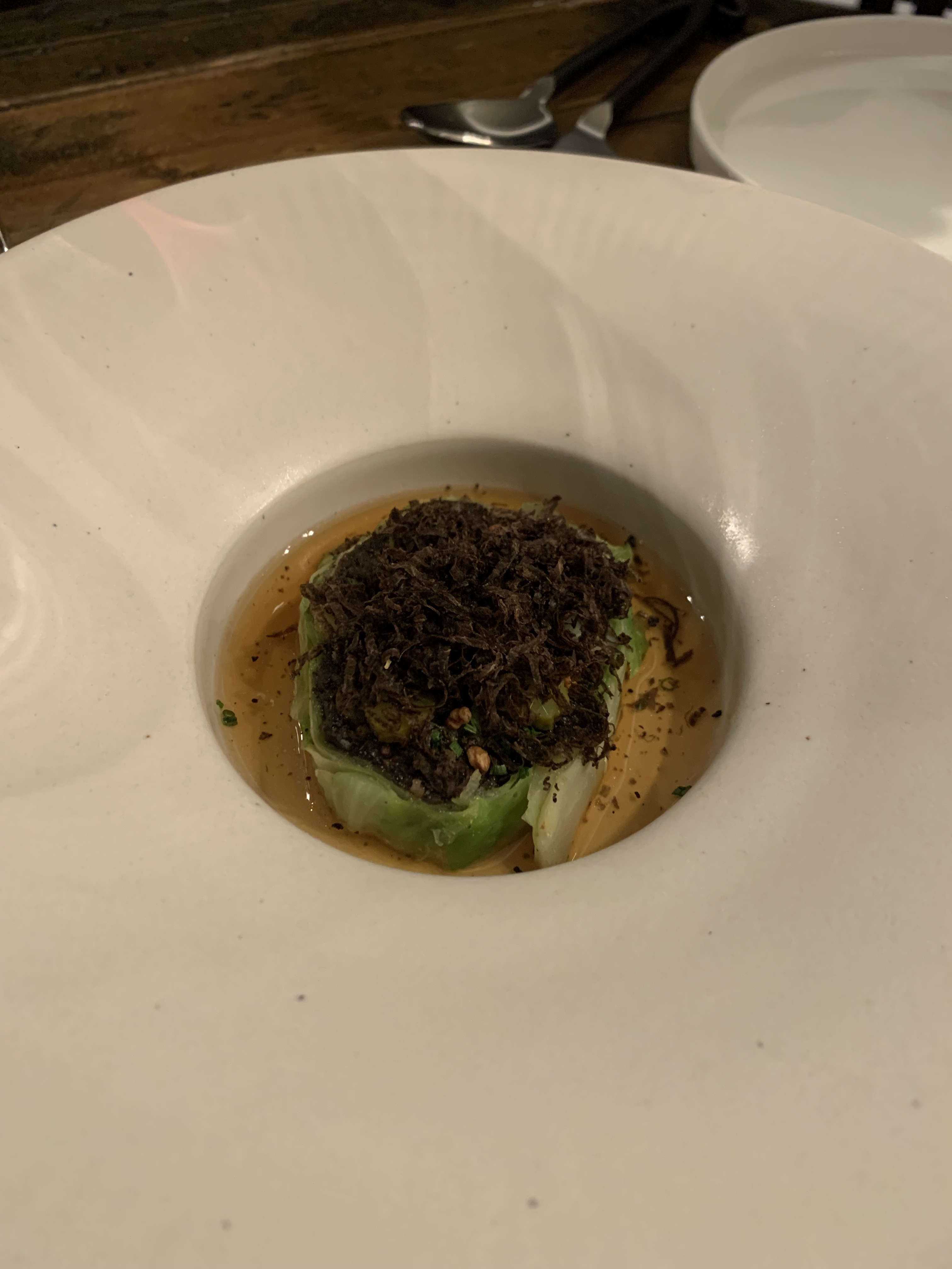 Heap of shaved truffle on top of some cabbage, with a light brown broth around it