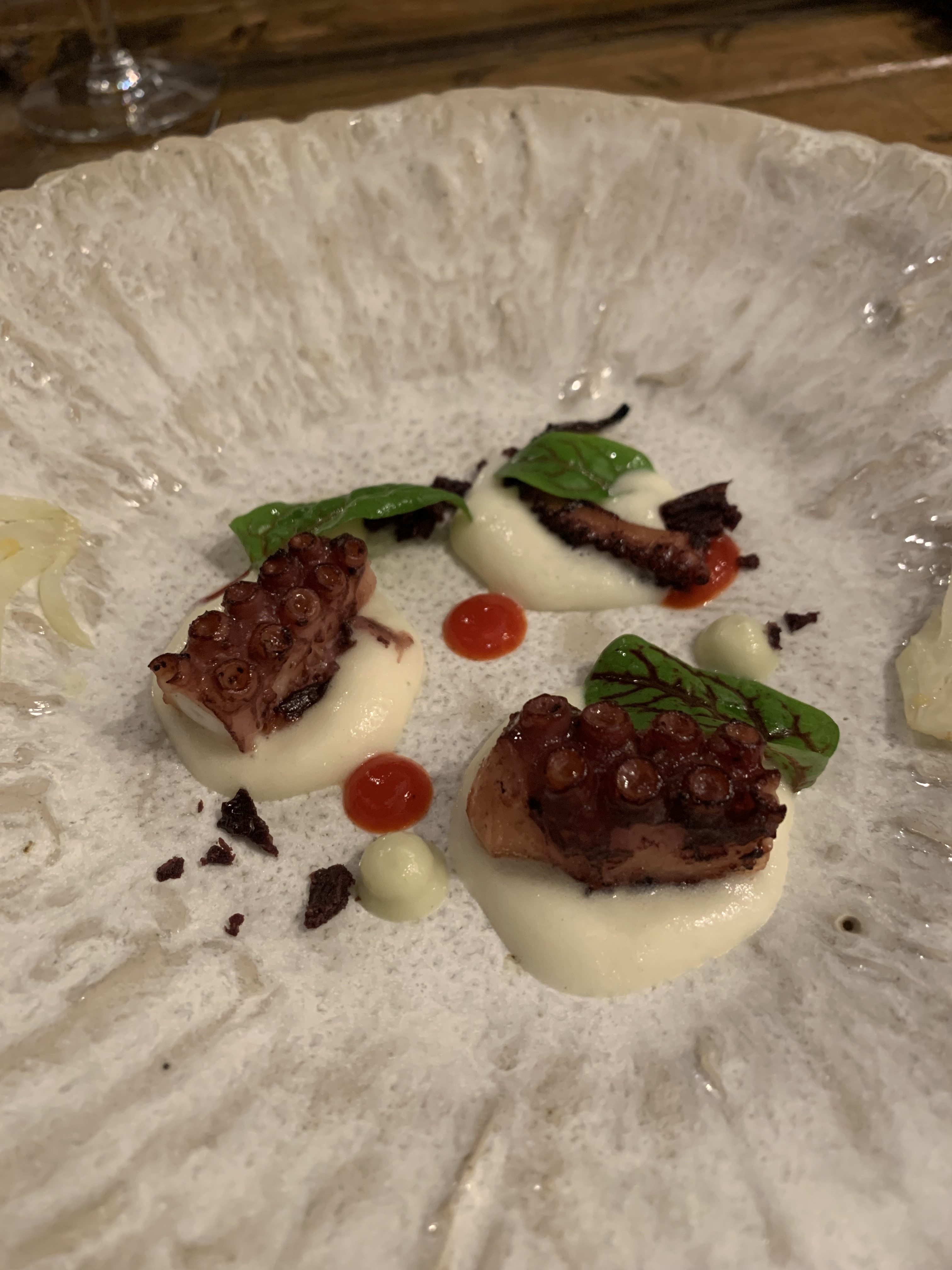 Chunks of octopus tentacle on their own dollop of white foam, with red dots and some greens scattered around the plate too